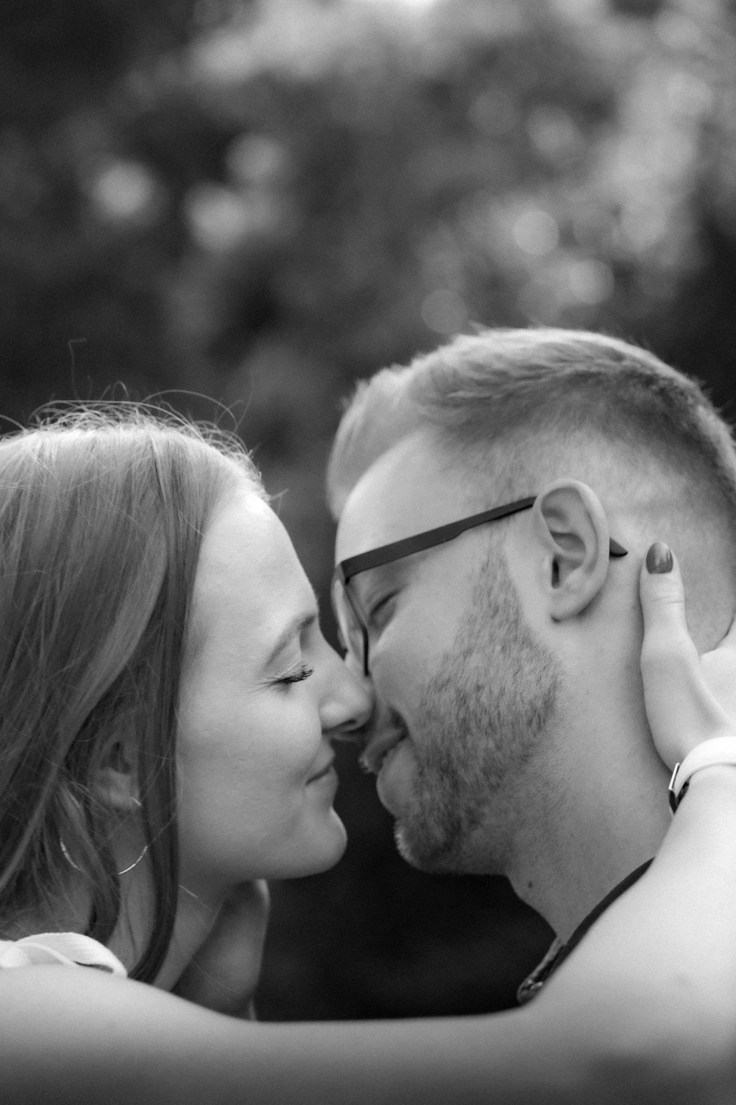 Ein Paar, das sich liebevoll berührt und Nähe zeigt, in Schwarz-Weiß. Sie lächelt, während er mit Brille und Bart ihre Stirn berührt.