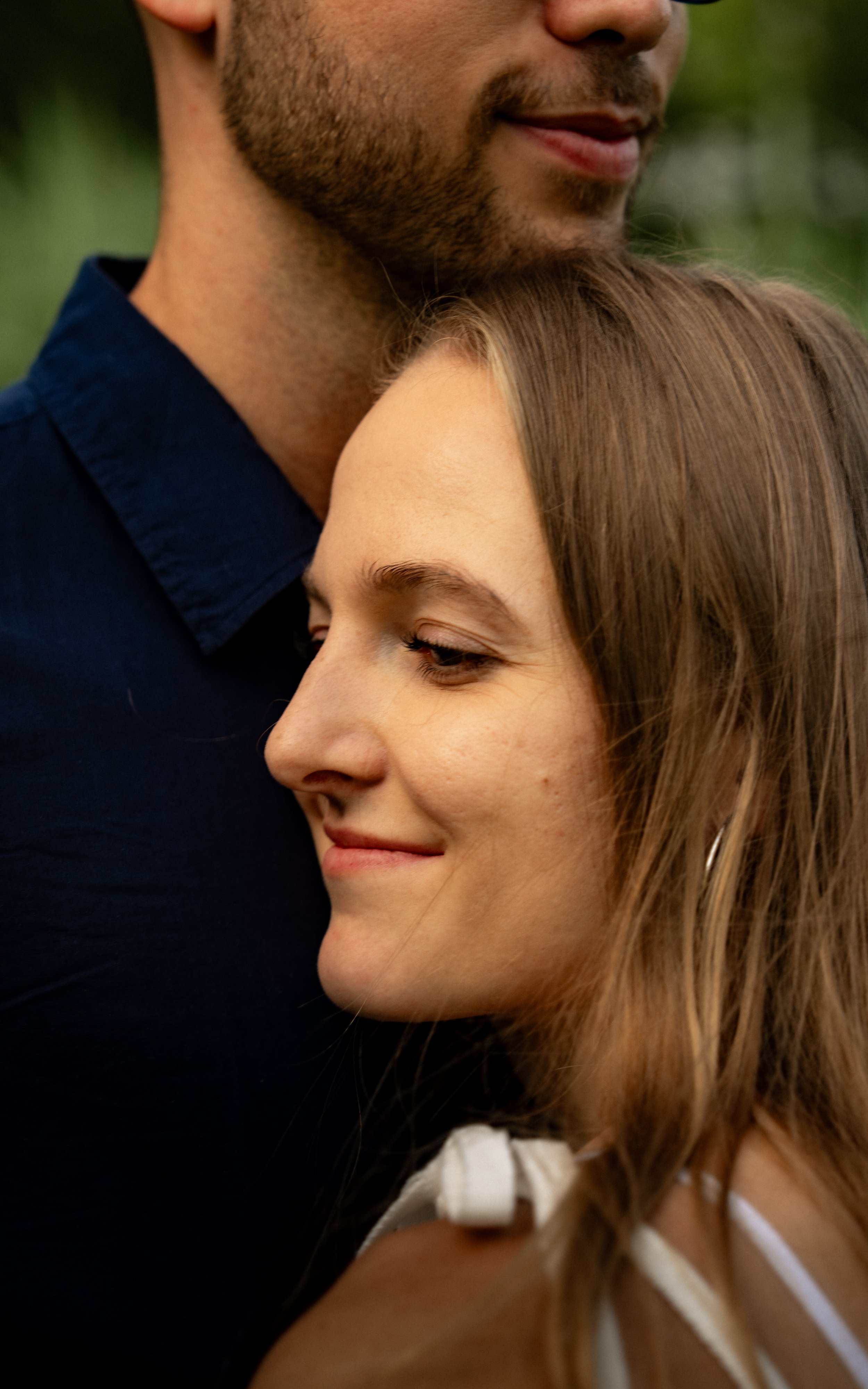 Ein Mann und eine Frau umarmen sich eng, sie lächeln und wirken glücklich, im Freien mit unscharfem grünen Hintergrund.