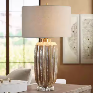 Decorative table lamp with a beige shade and a textured, metallic base on a wooden surface.
