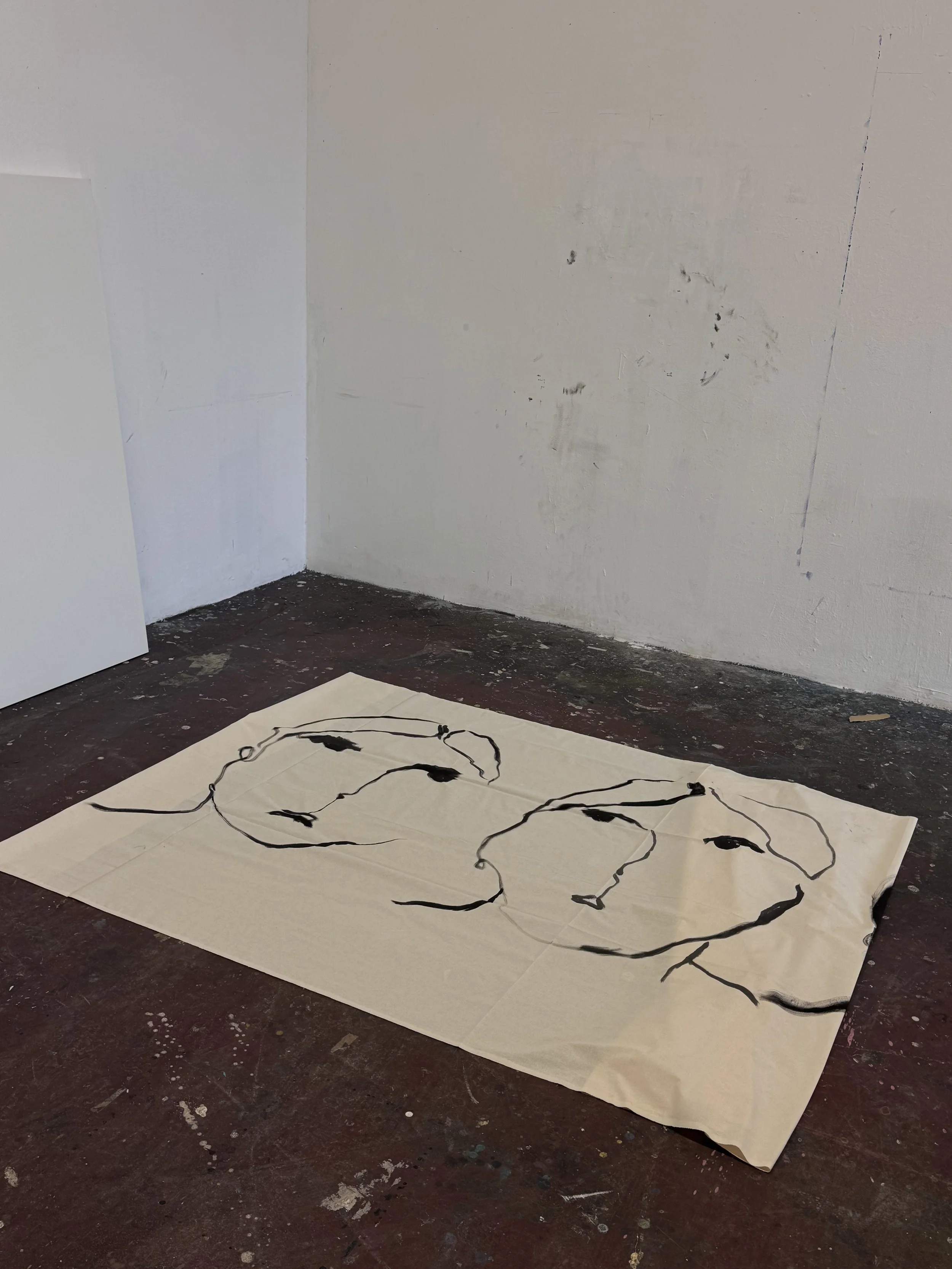 A large sheet of paper with black abstract line art on a brown floor in an art studio, walls are white with some scratches and marks.