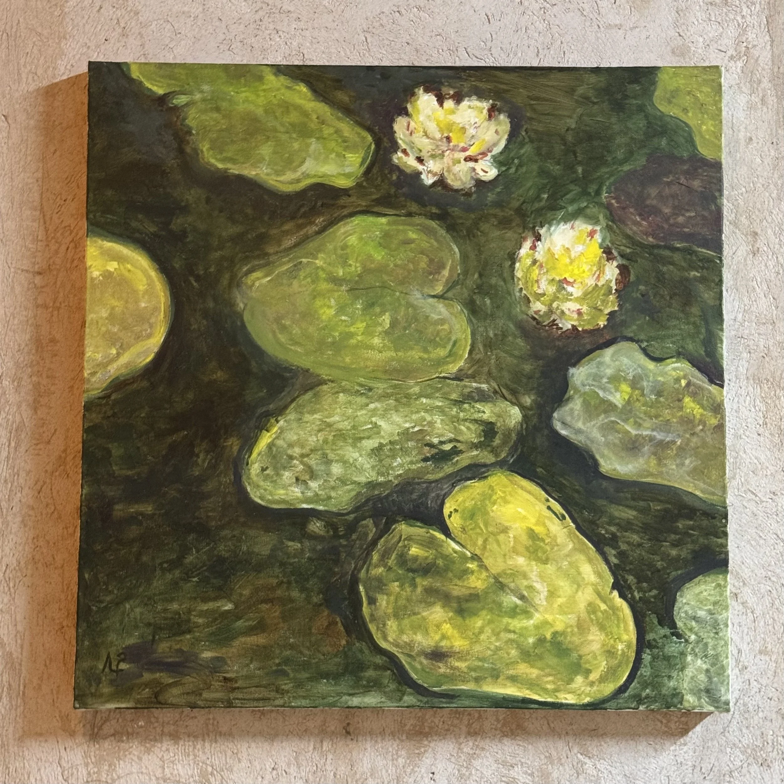 An impressionism painting with green, yellow, and white colors water Lillies on a rectangular canvas placed on a textured light-colored surface.