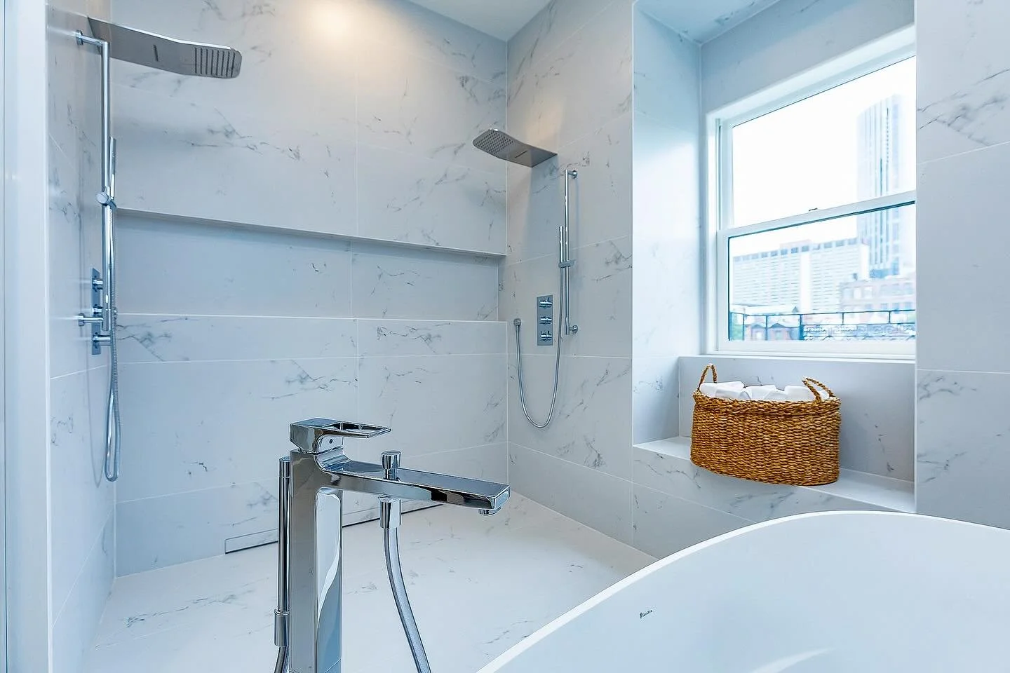 Where serenity lives. This space blends floor to ceiling porcelain tile from @porcelanosa_us with a generous custom niche made for every self care essential. The stone resin soaking tub from @bainultra invites slow moments, while sleek @hansgrohe_usa