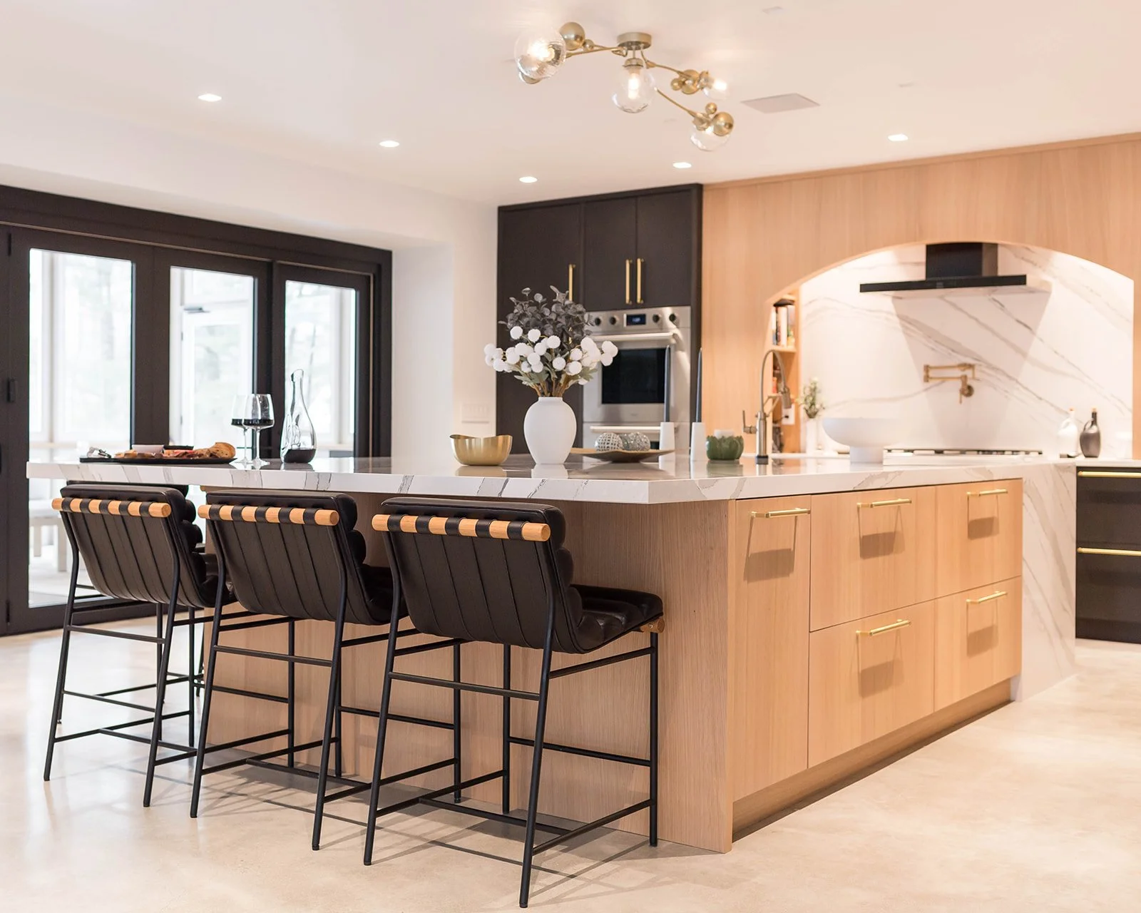 After photo of renovated kitchen with large center island, pendant lighting, and expansive Marvin Doors bringing in natural light.