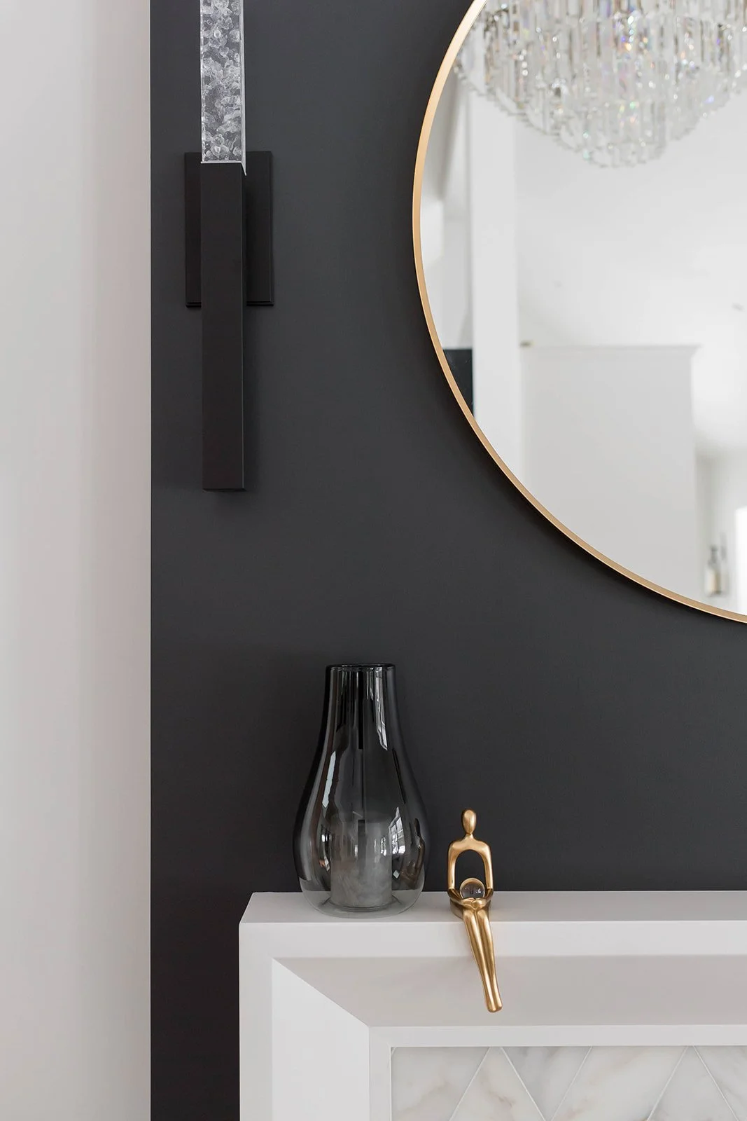 Modern interior design with a round mirror, black wall sconce, black vase, and gold figurine.