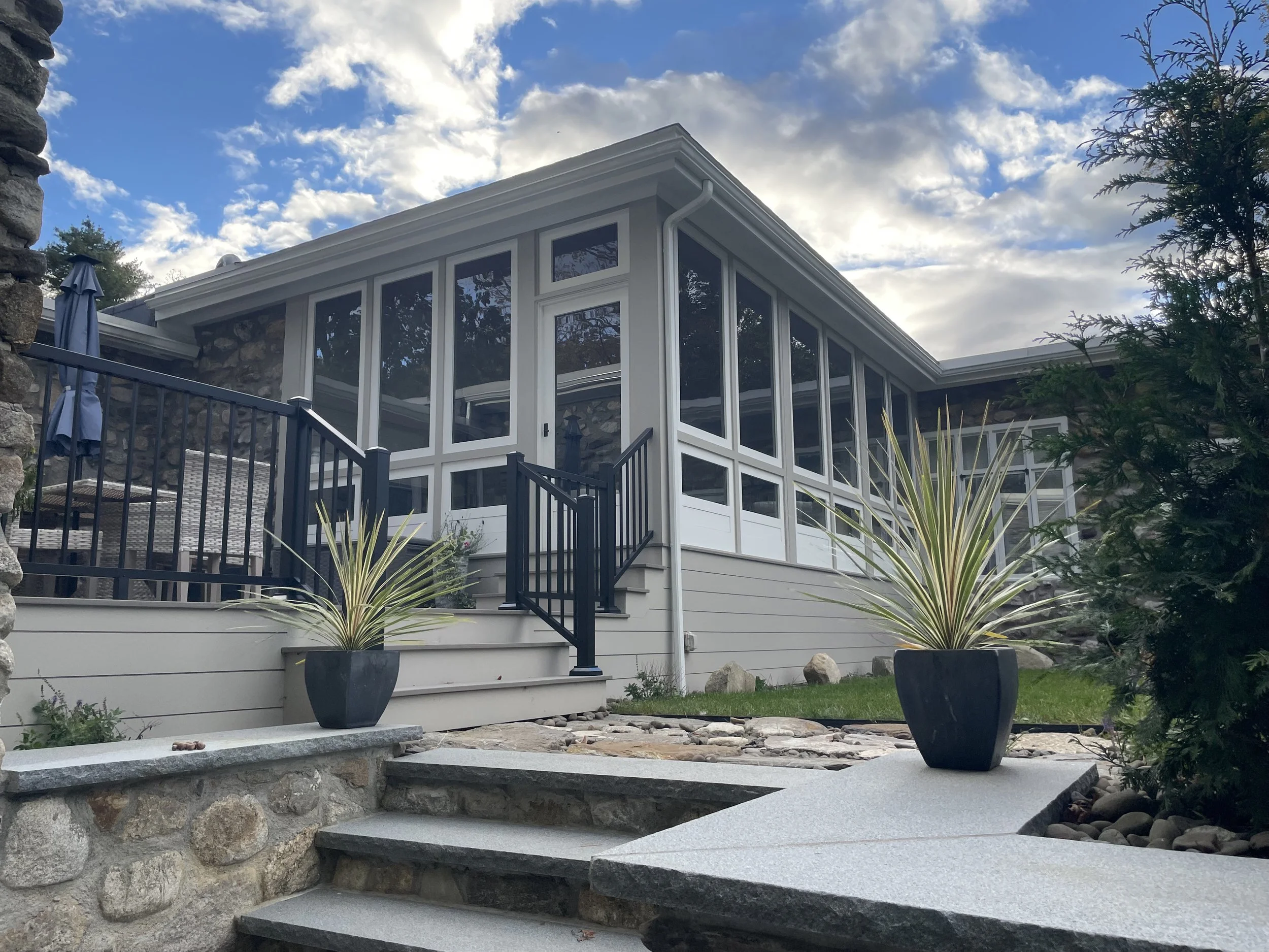 3 Seasons porch with a lower deck, granite caps, new fieldstone wall, new hardscape and landscaping for a serene outdoor space.