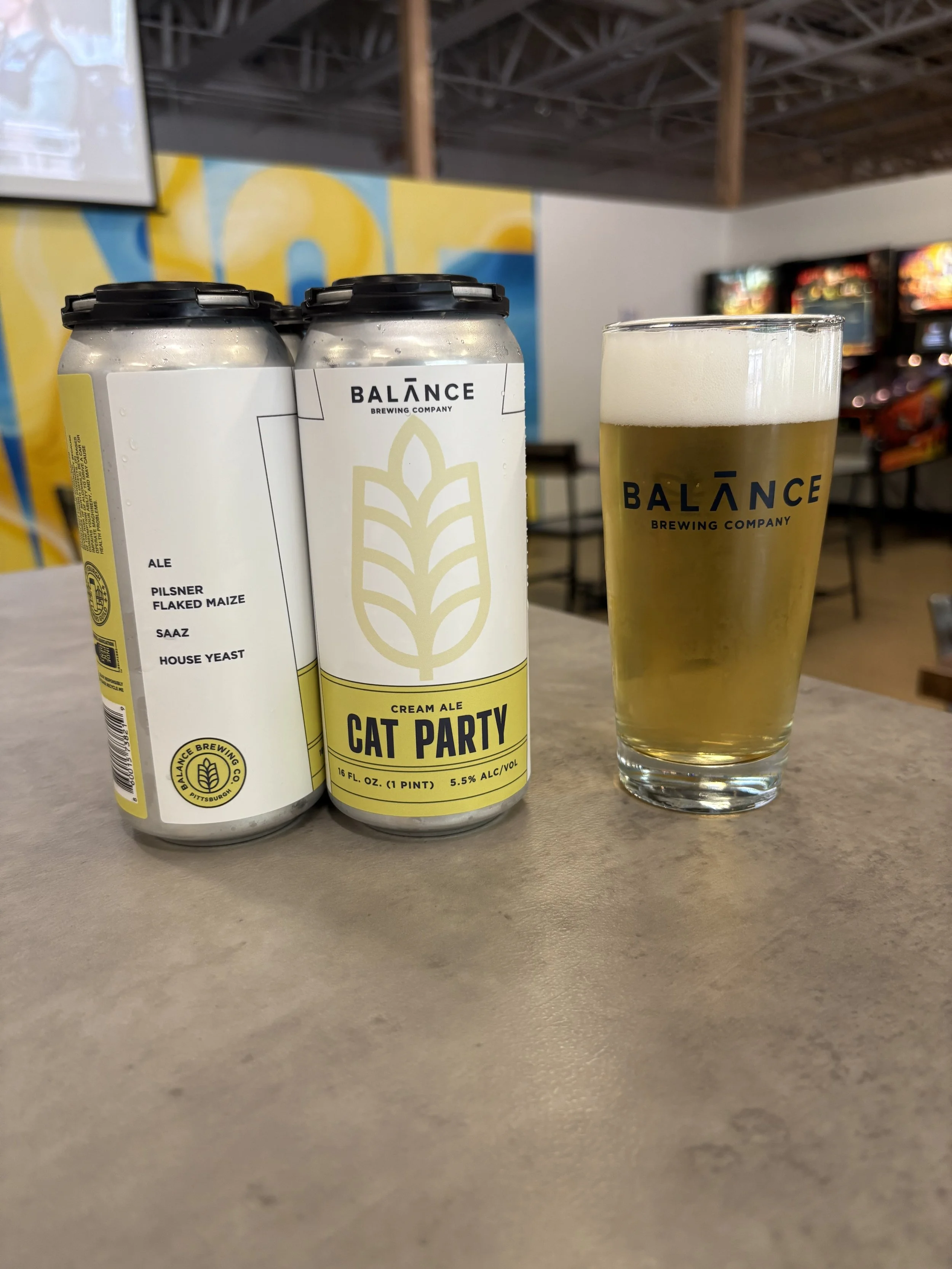 Beer cans with a white kitten sitting on top of the cans. 
