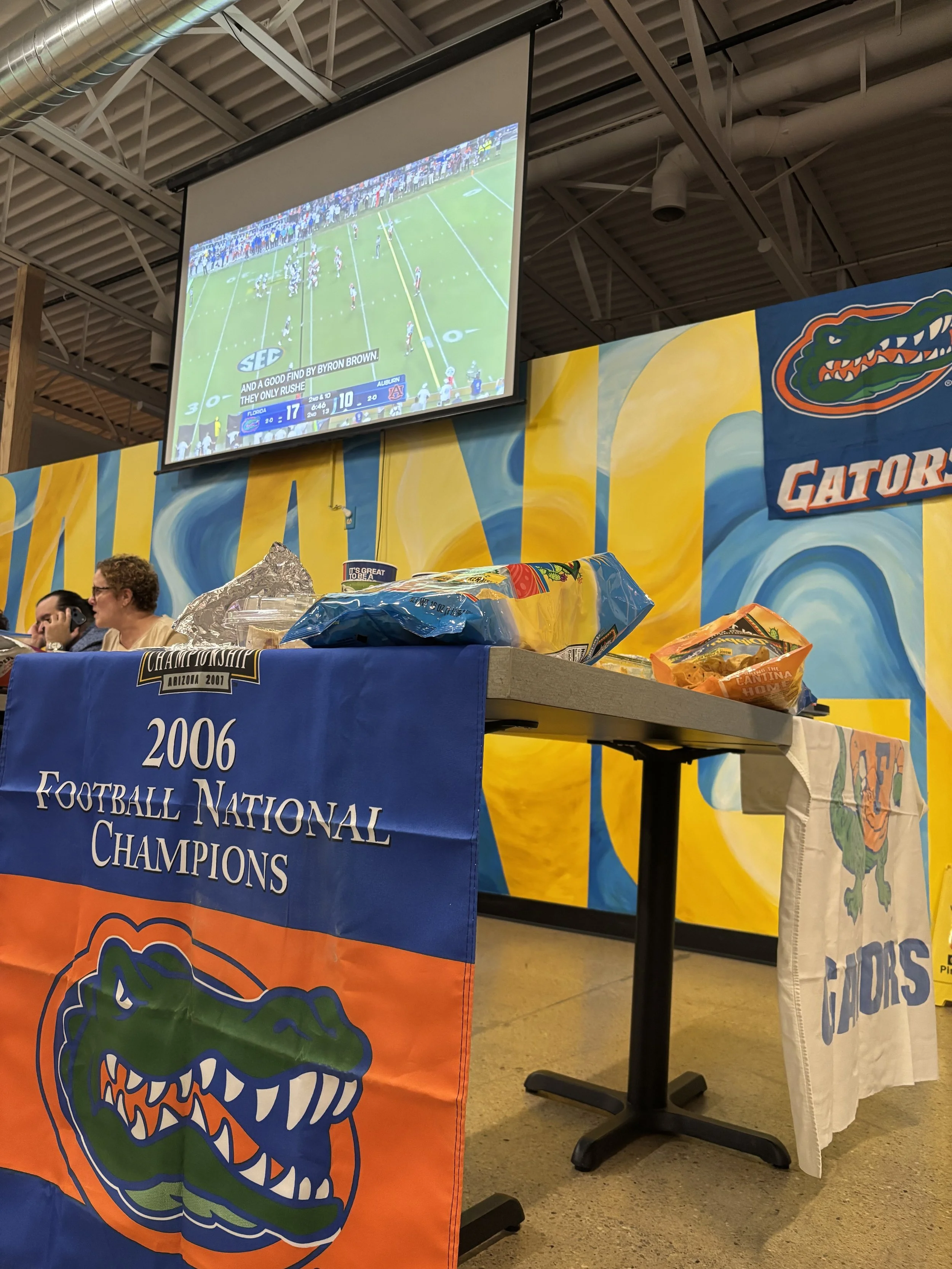 Image of large screen projector of a football game in the background, closeup of a Florida Gators banner in the foreground