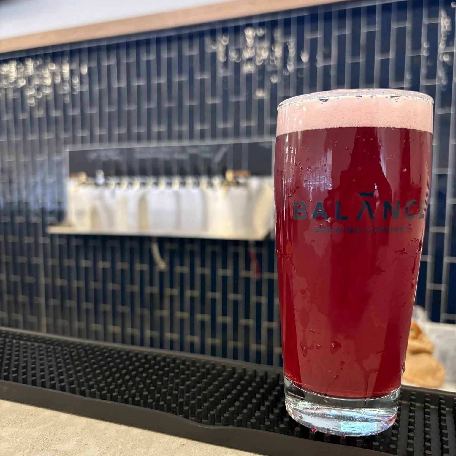 A full glass of a dark pink beer against a blue tile backsplash. 