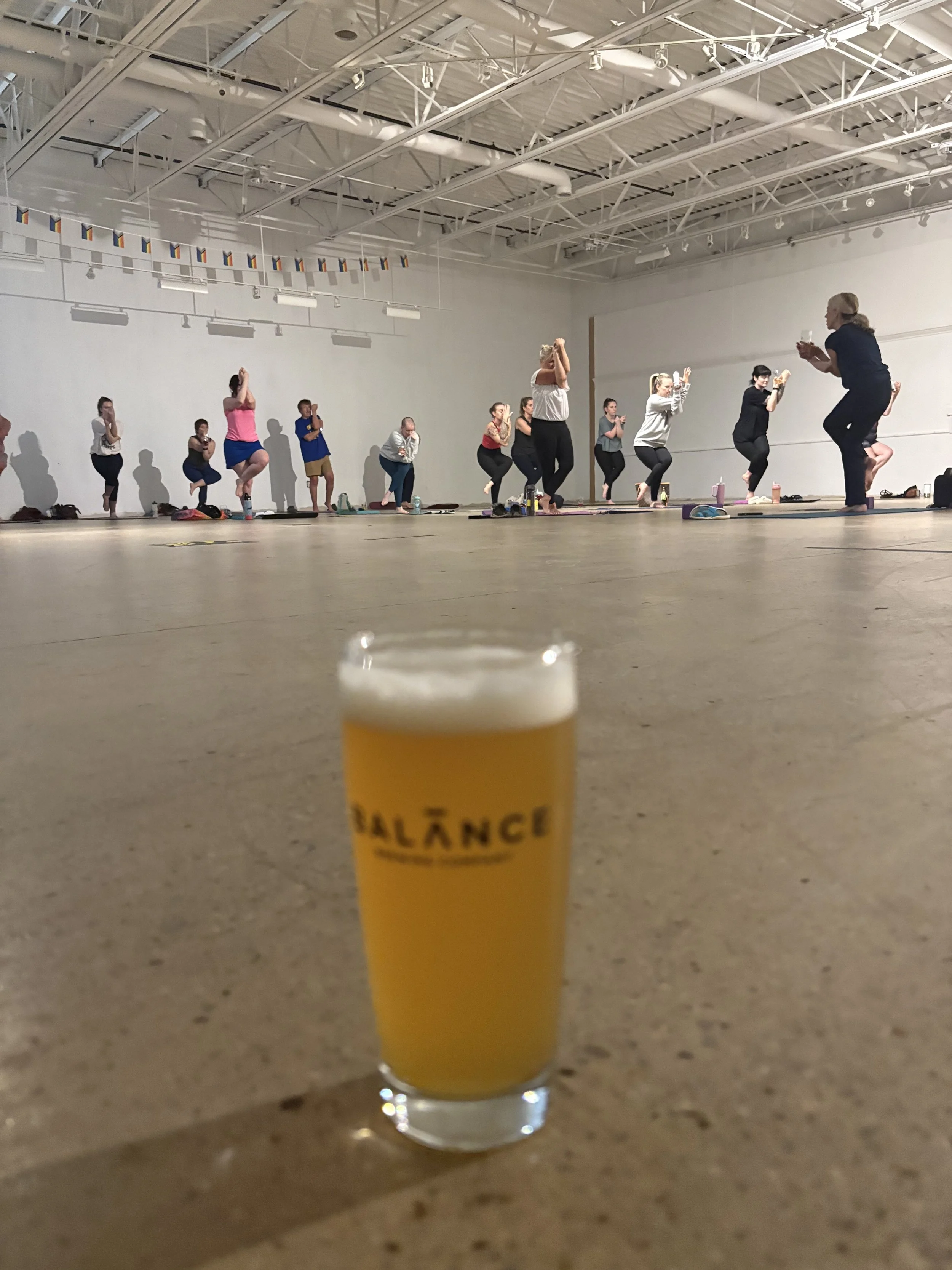 Image of a glass of beer in the foreground and a group of people doing yoga in the background