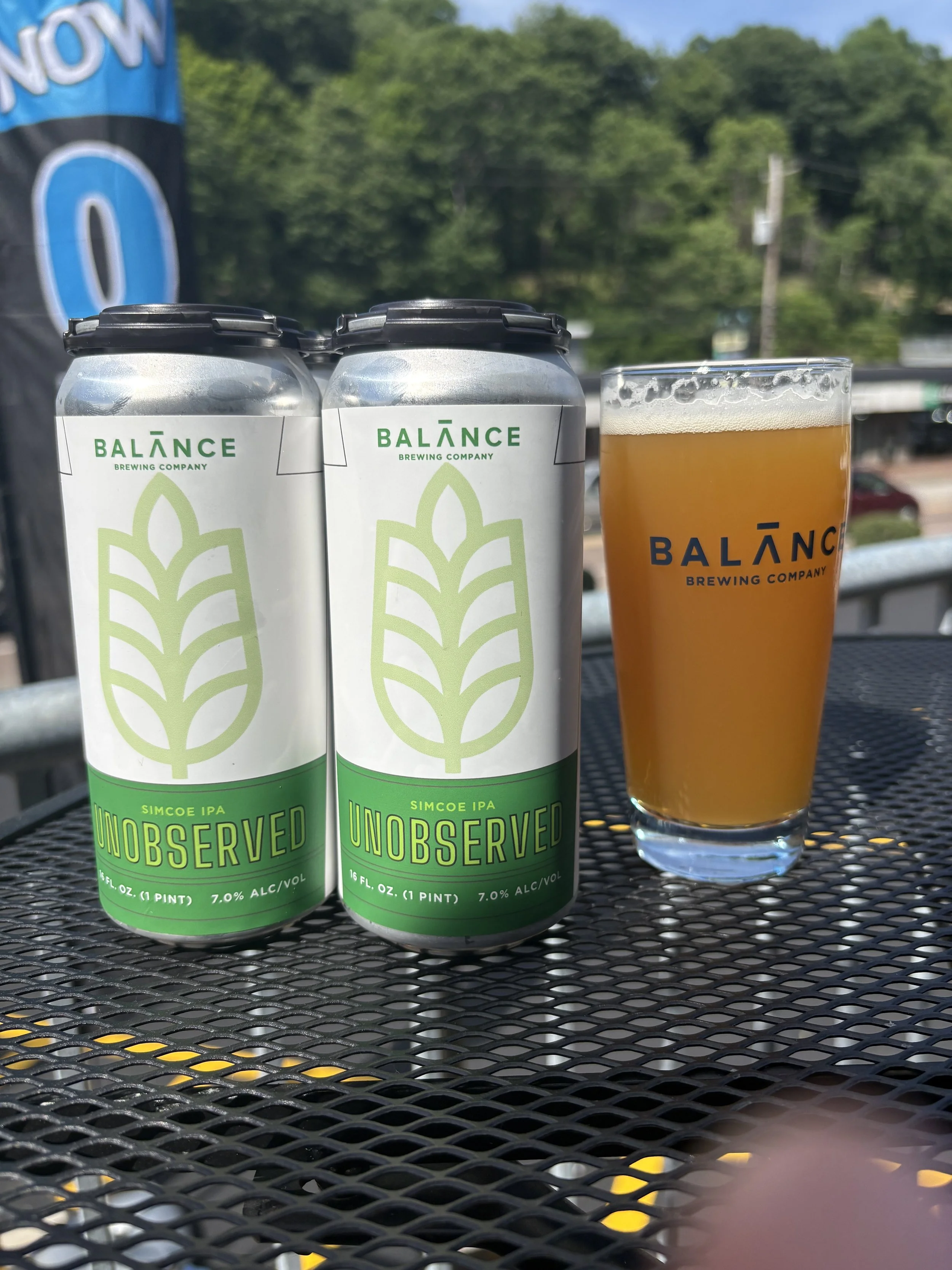 Cans of beer with green label, next to orange beer in a glass.