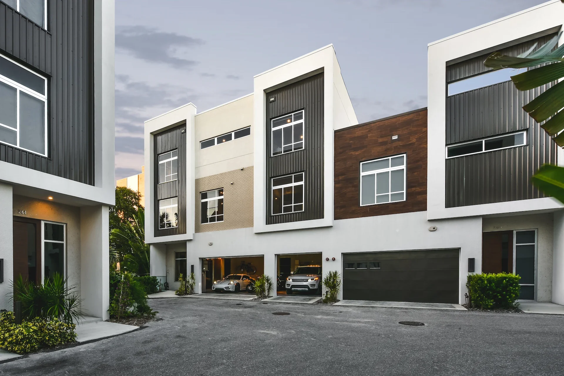 Modern multi-story residential building with garage doors, black and white exterior, and landscaped surroundings.