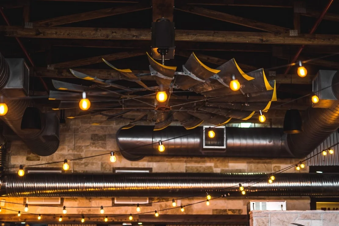 Texas inspired ceiling, using a reclaimed windmill as a ceiling fan, string lights, exposed ductwork, and hill country inspired materials.