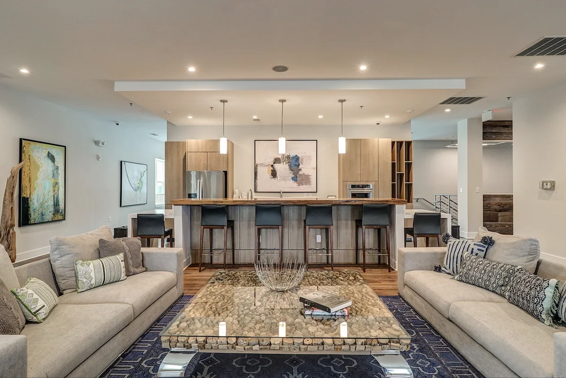 Modern interior staircase in a bright open floor plan with white walls, large windows, and decorative rocks and plants in the foreground.