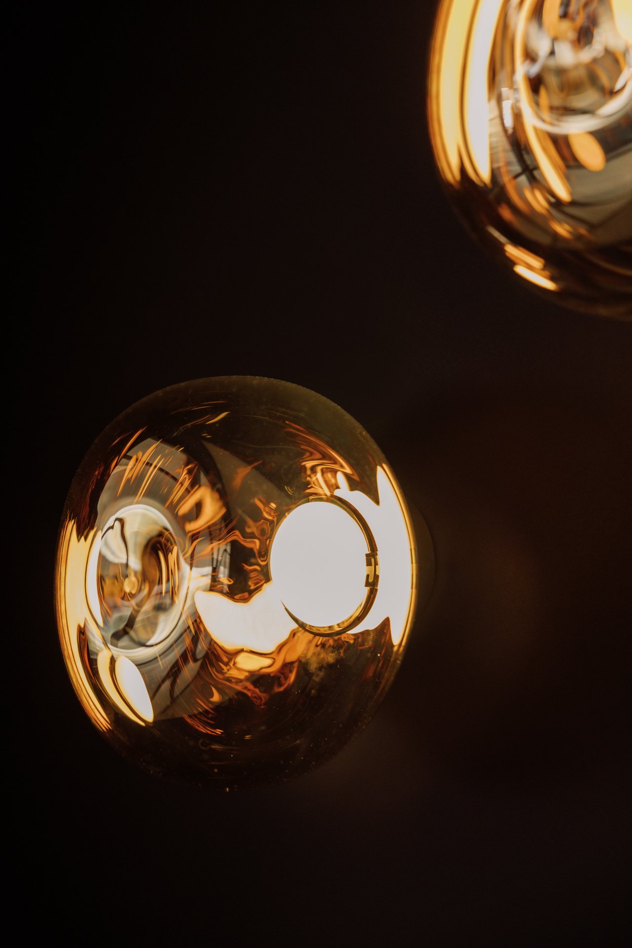 Close-up of two transparent, glass orbs with internal reflections and glowing amber-orange light, set against a dark background.