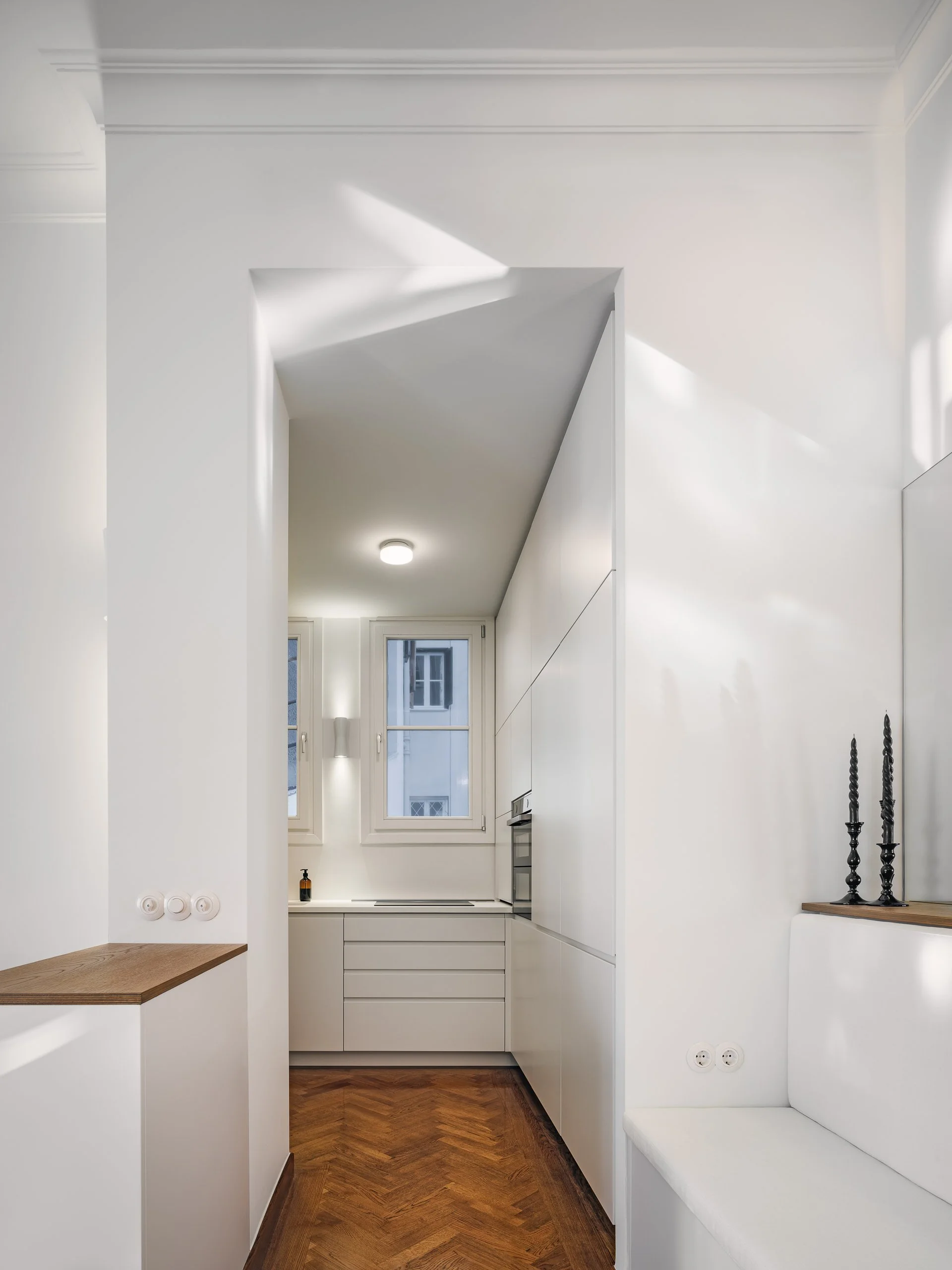 Minimalist white kitchen with two windows, wooden parquet floor, and simple cabinetry