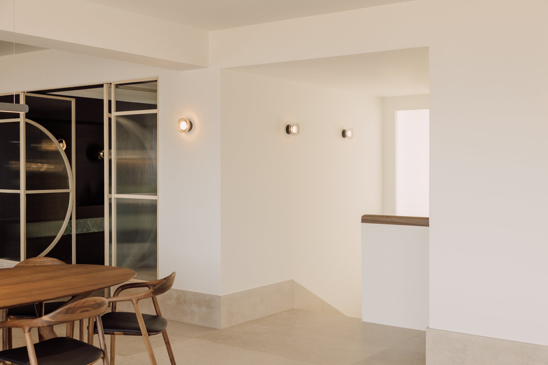 Minimalist dining area with a wooden table, chairs, and modern wall lights in an open-concept space with natural light.