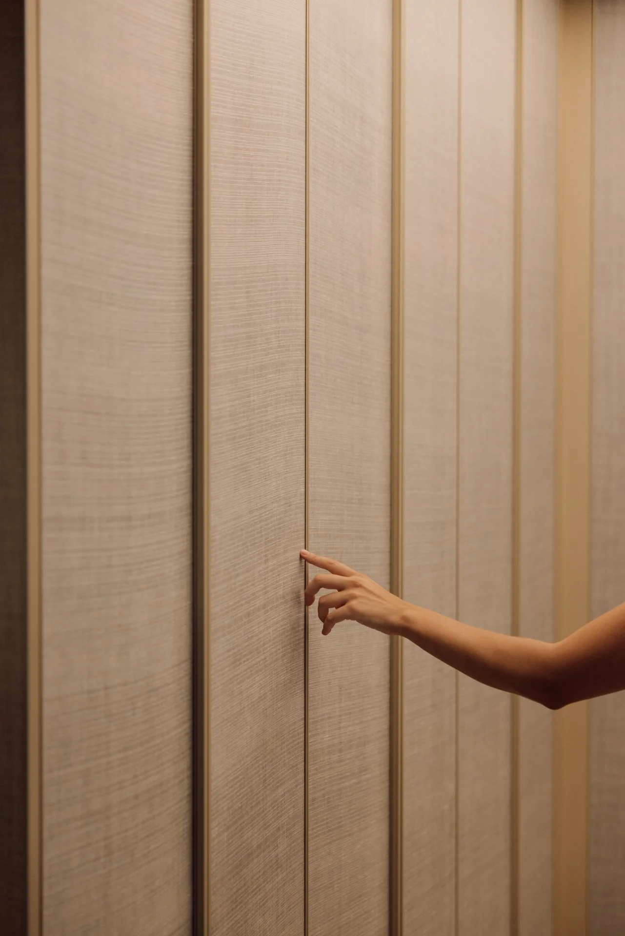 A person reaching out with their hand to open a wooden door in a modern interior.