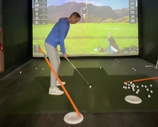 A person practicing golf swing in an indoor simulator with a large digital screen displaying a golf course and mountains.