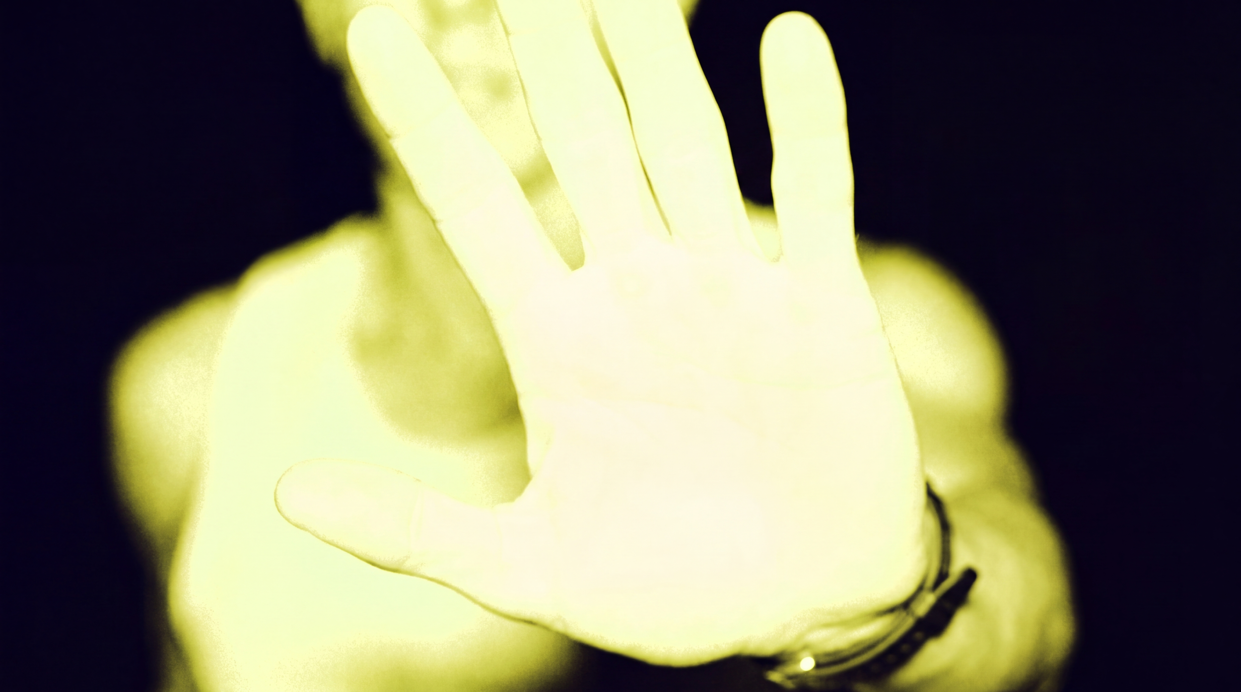 Close-up of a hand illuminated with yellow light, with fingers partially visible against a dark background.