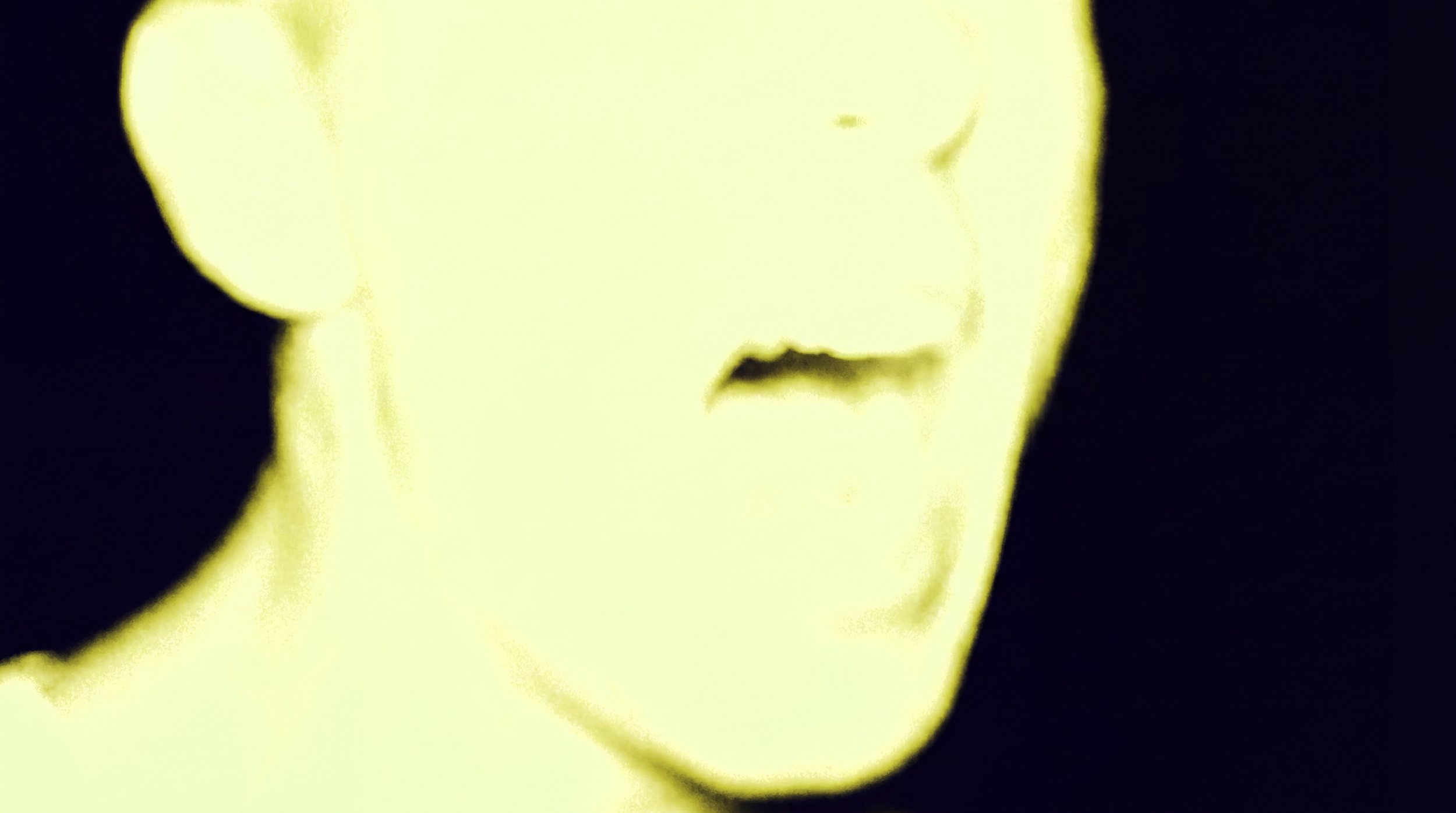 A close-up, abstract and blurry image of a human face with only the lips and part of the nose visible, predominantly in yellow and black colors.