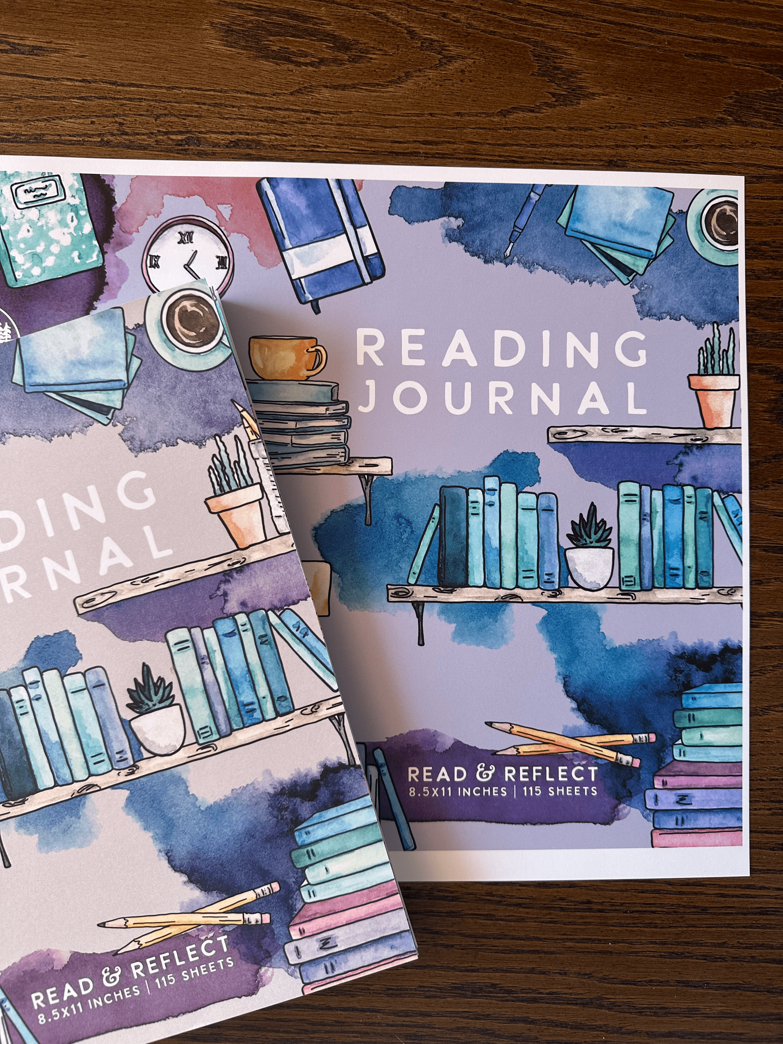 Cover of a reading journal with watercolored illustrations of books, plants, a clock, pencils, and coffee cups on a wooden surface.