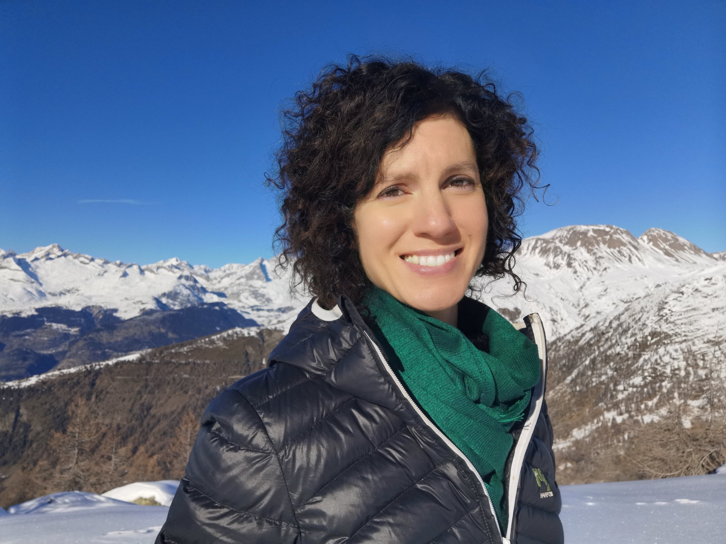 Melanie Shudofsky from Leadership Coaching Outdoors standing outdoors amid the snow-capped mountains and blue sky