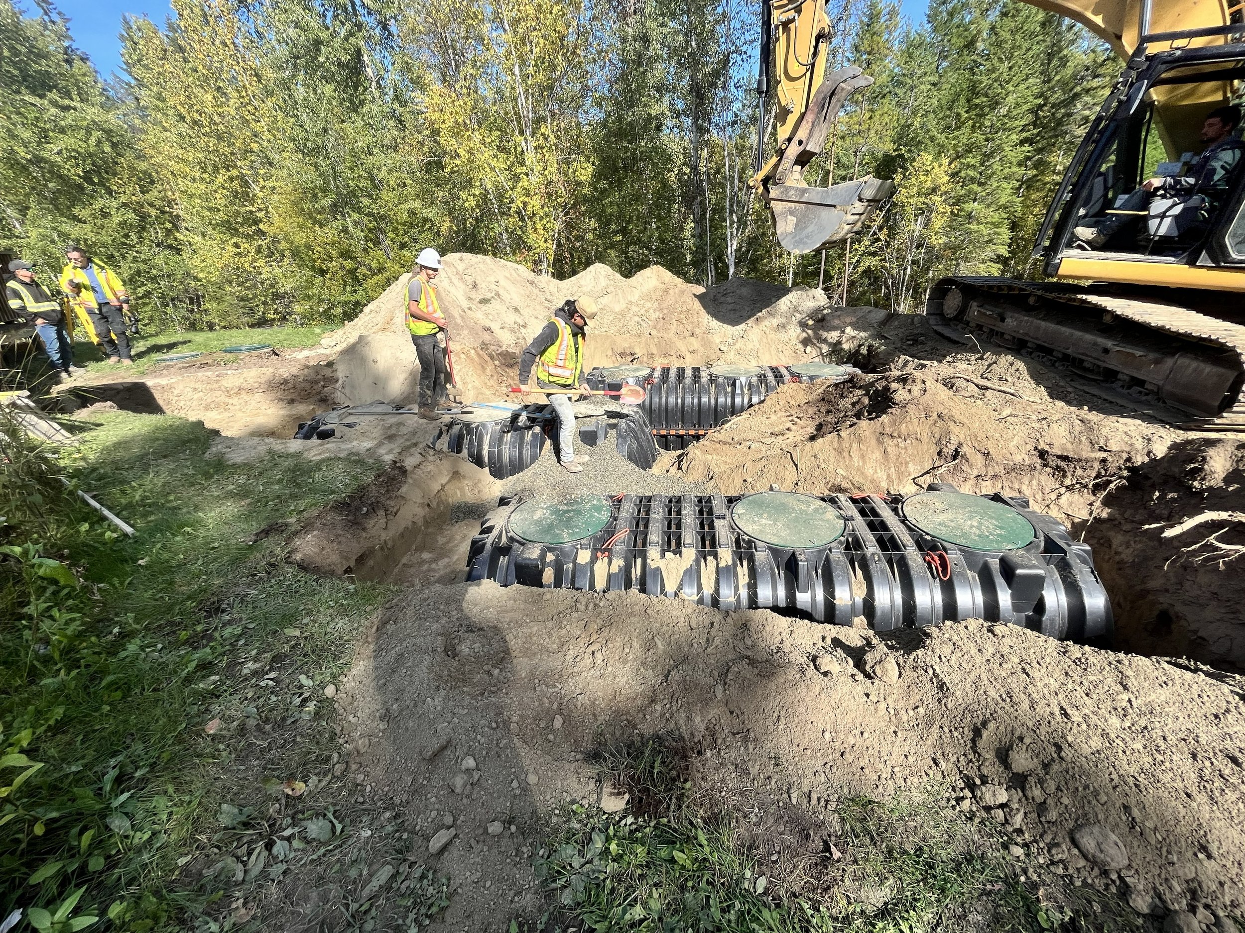 Construction workers and an excavator installing two large septic tanks for a community wastewater treatment system.