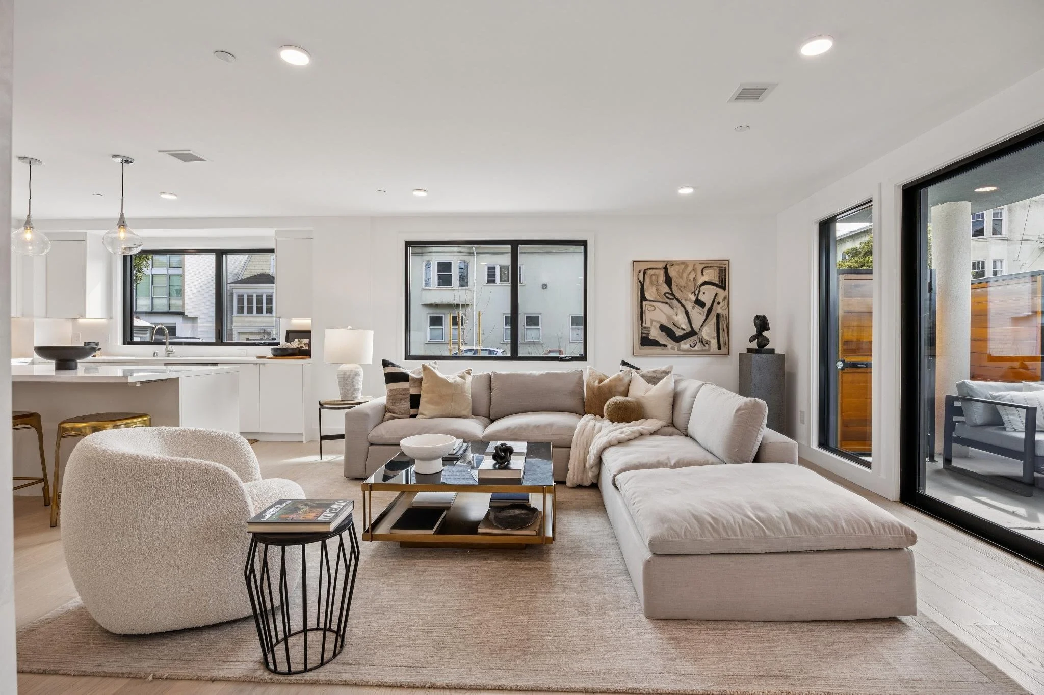Modern living room with white sectional sofa, beige armchair, glass coffee table, and large windows.