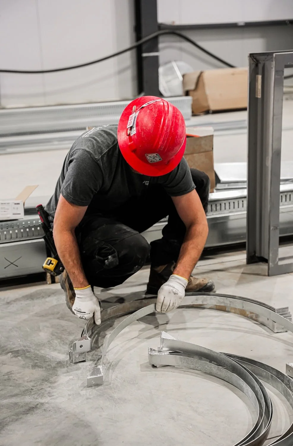 Un homme portant un casque de sécurité rouge et des gants travaille à l'intérieur d'une structure métallique, utilisant une échelle pour atteindre une partie supérieure de l'installation.