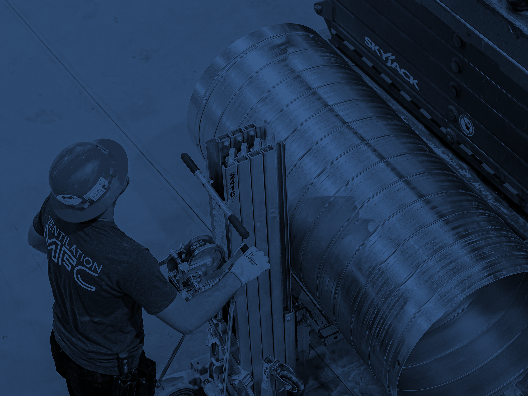 Un technicien portant un casque de sécurité et un uniforme travaille sur une grande conduite en métal dans un environnement industriel. L'image met en évidence la sécurité et la maintenance de l'infrastructure.
