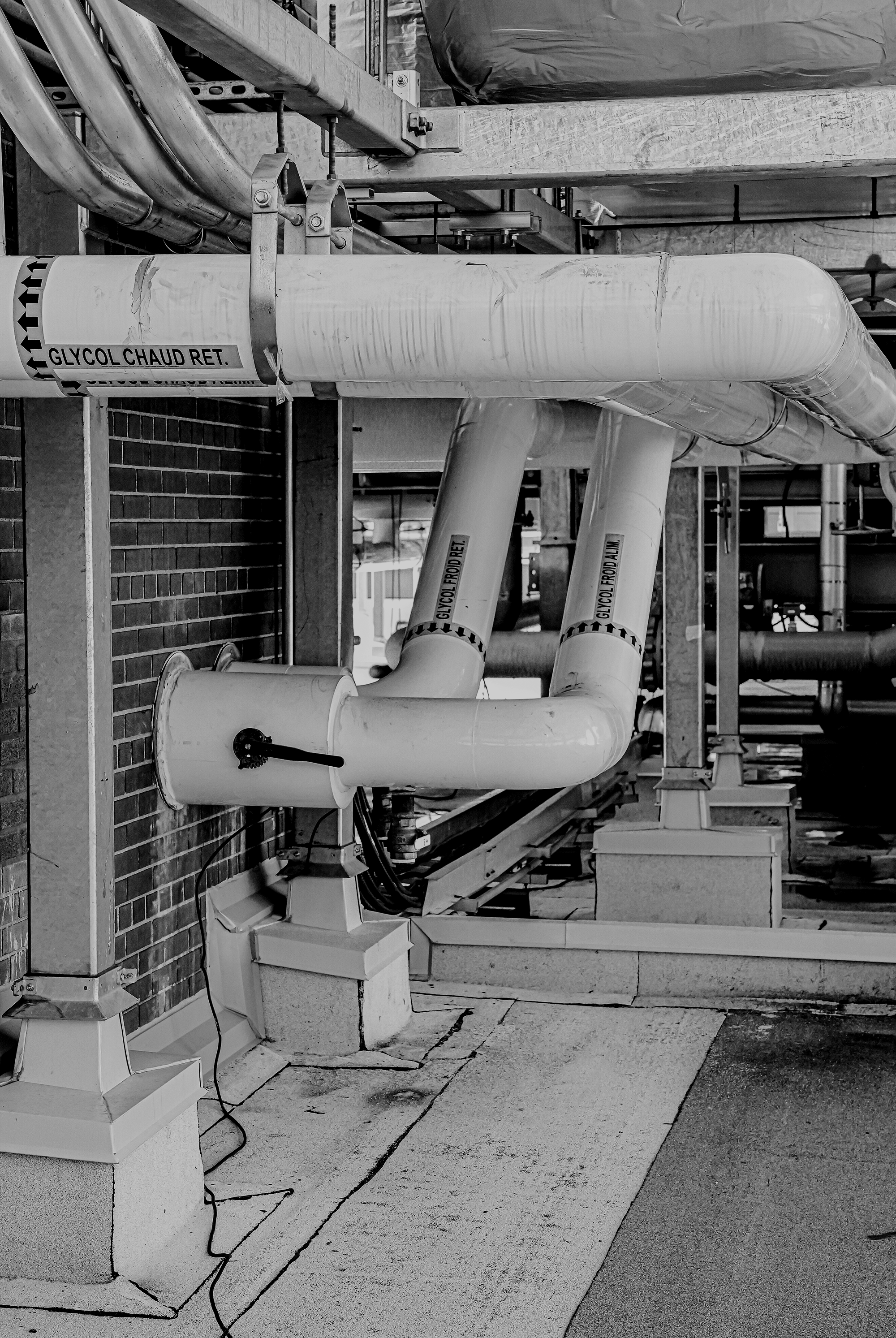 Tuyaux de plomberie isolés avec étiquettes, installation industrielle sur un toit ou un bâtiment, en couleur noire et blanche.