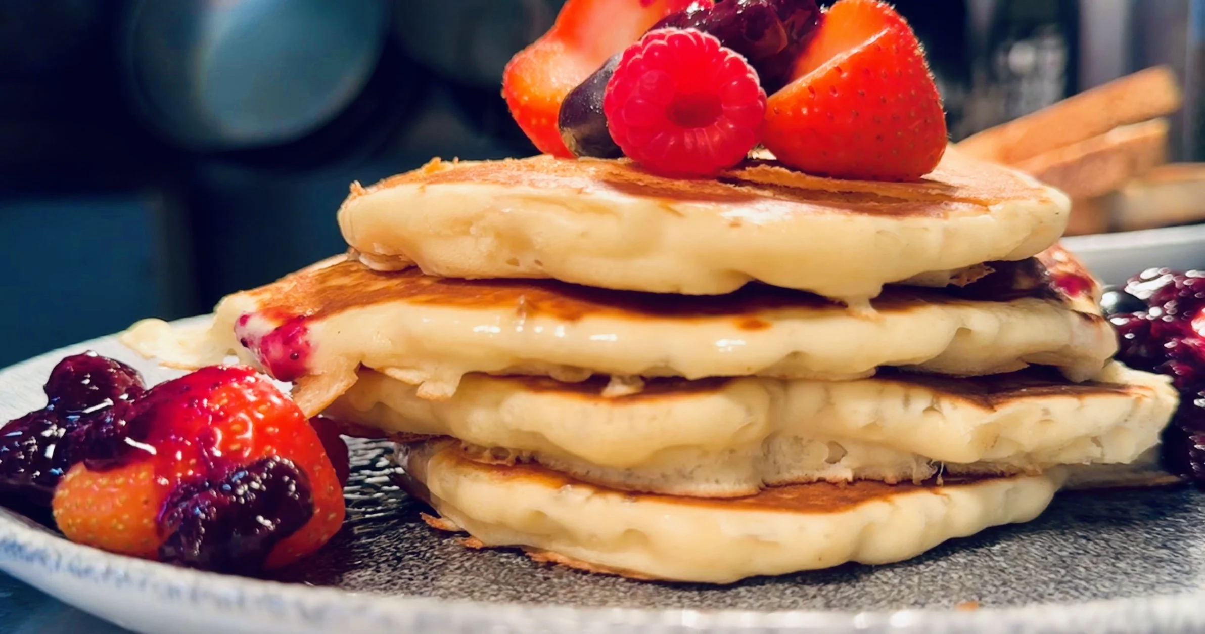 Stack of pancakes topped with strawberries, raspberries, and blueberry sauce.