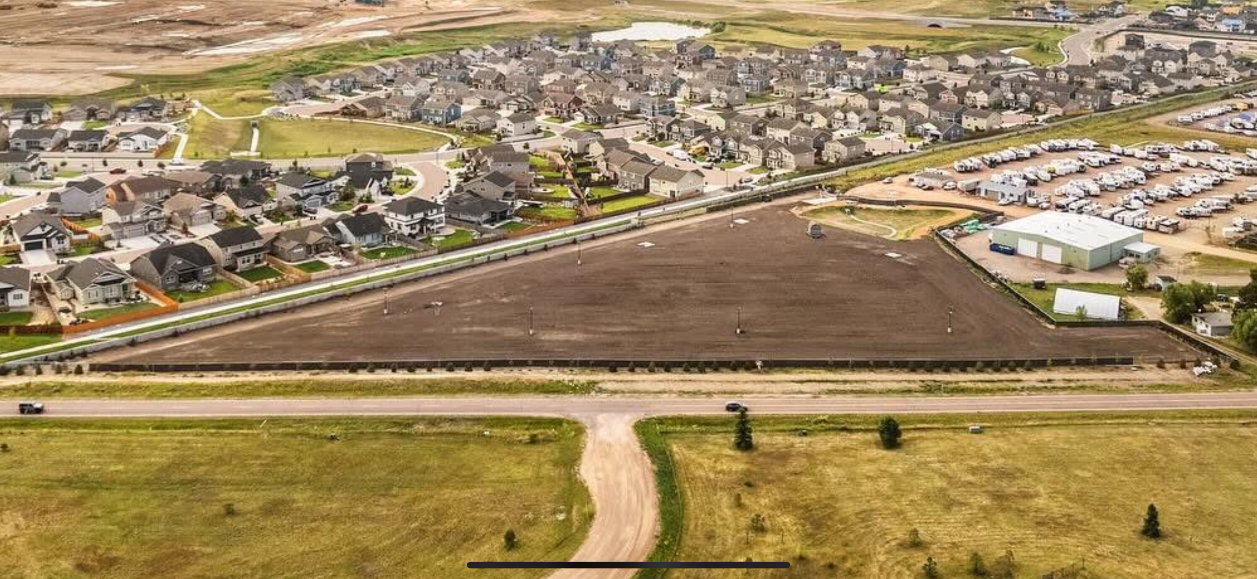 Aerial view of a suburban neighborhood with a large empty lot in the foreground, surrounded by houses and a parking lot.
