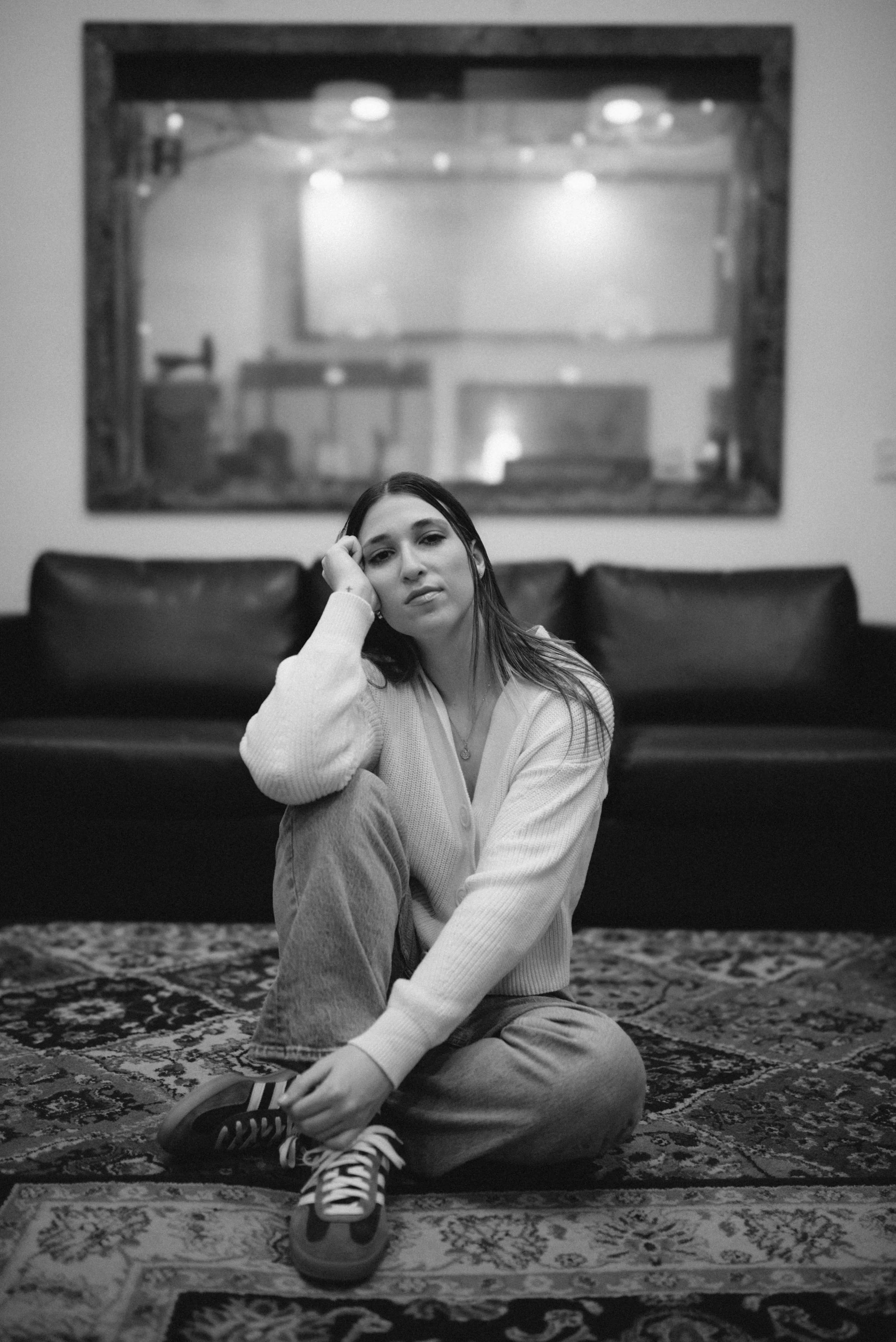 Black and white image of Julia DeTomaso seated on studio rug in live room— reflective, moody portrait.