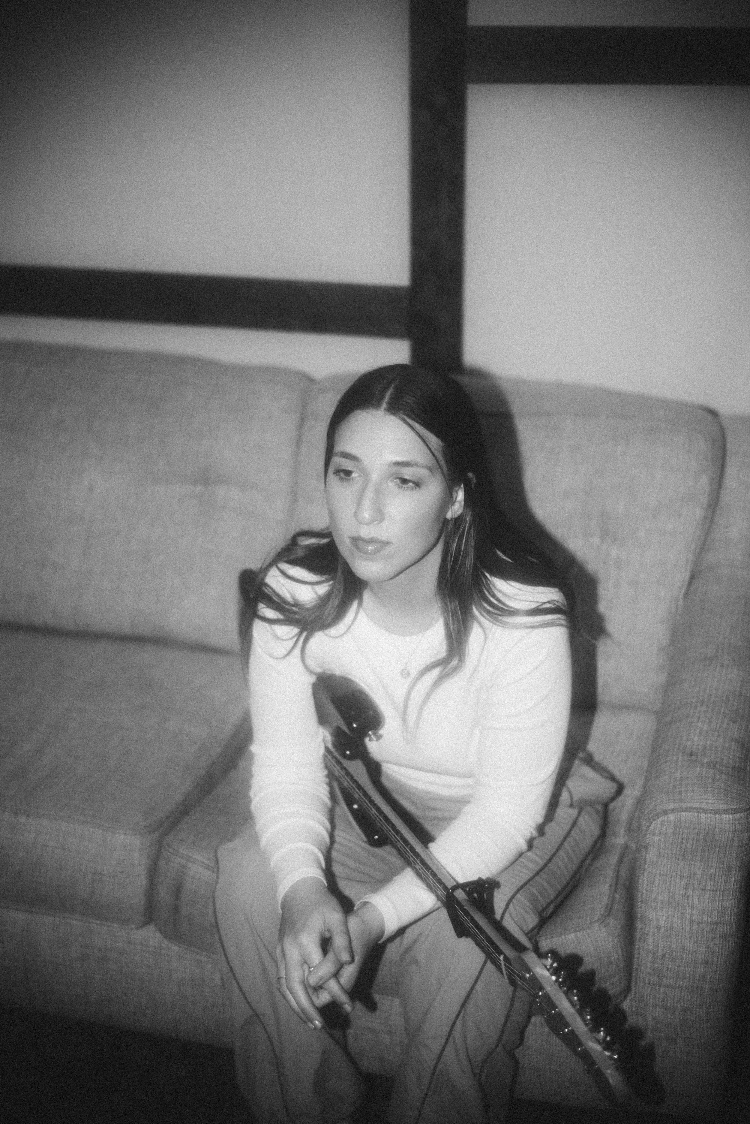 Black and white photo of Julia DeTomaso seated with electric guitar in lap, gazing off-camera — introspective session portrait.