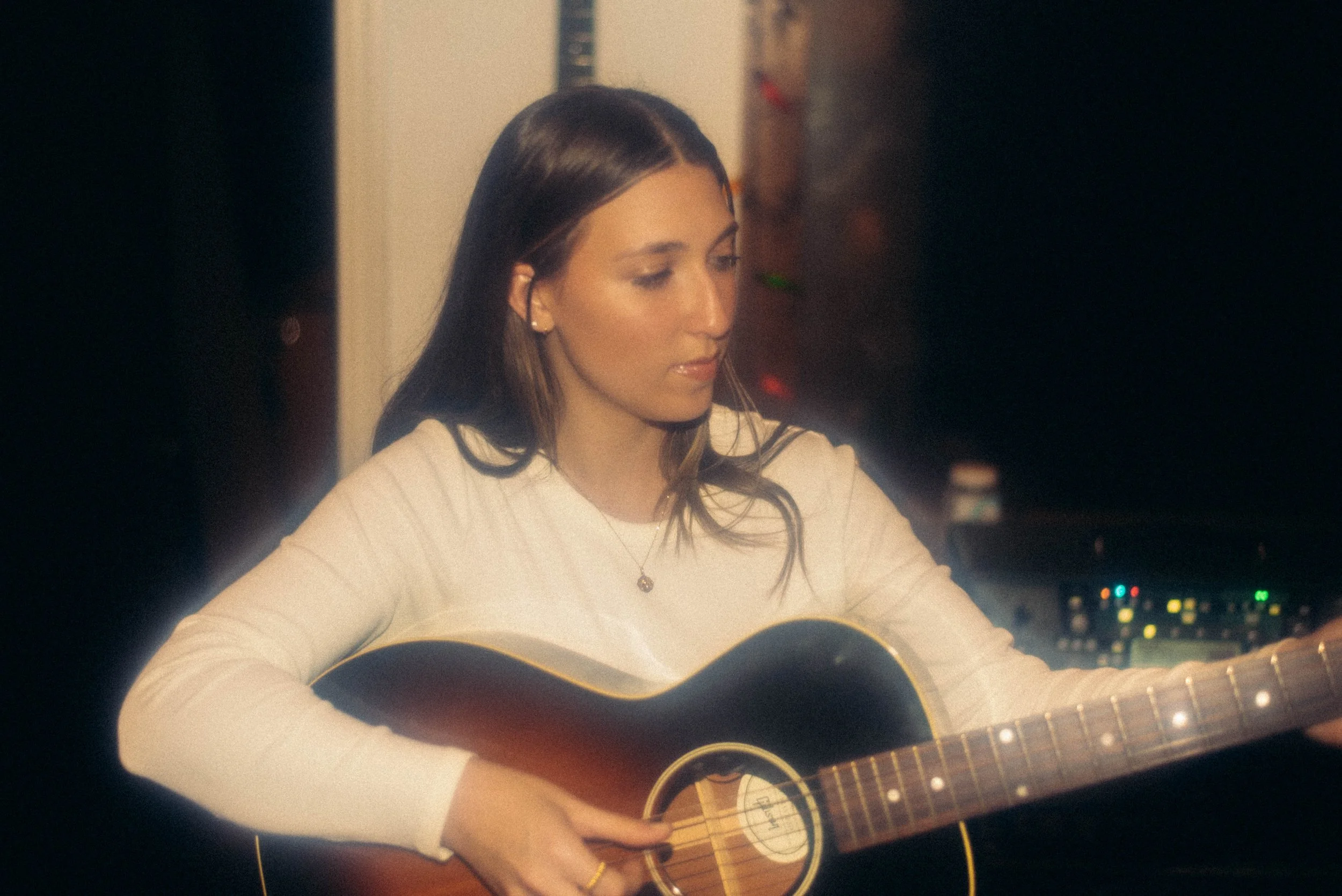 Julia DeTomaso performing acoustic guitar indoors — moody indie-pop session photo.