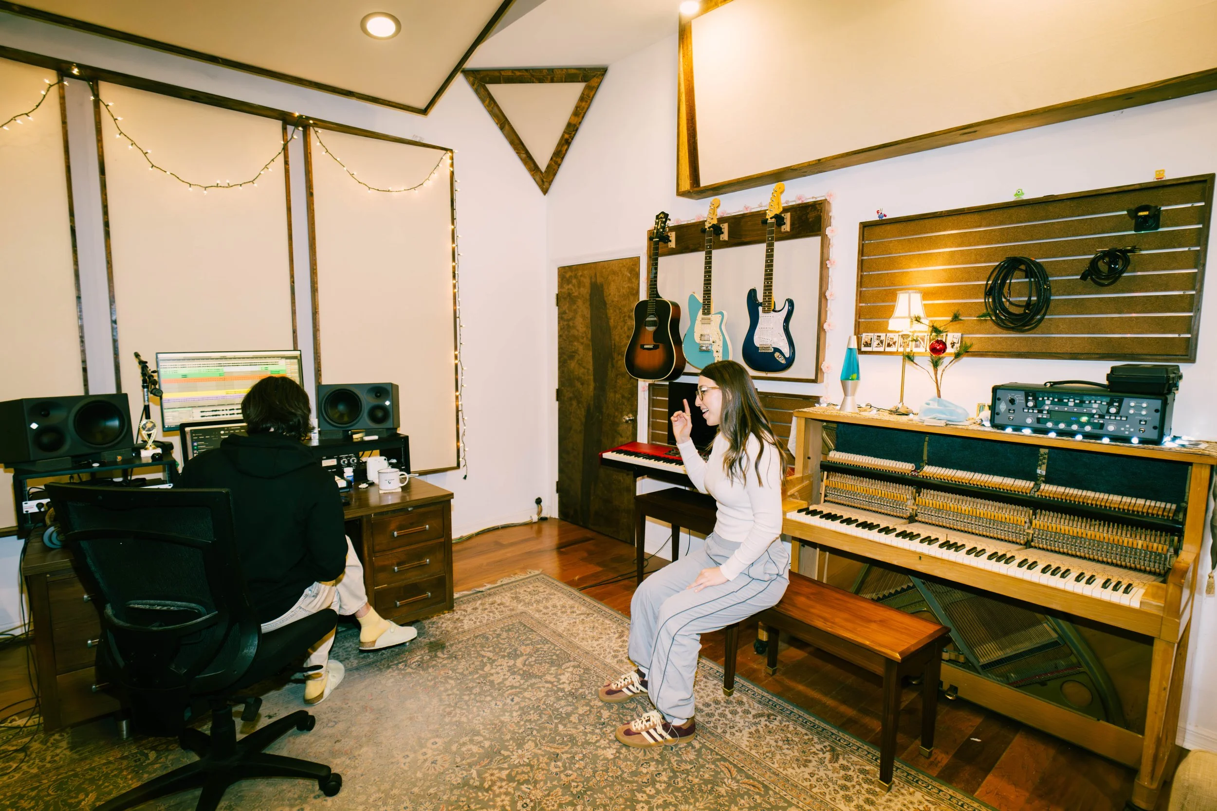 Julia DeTomaso in recording studio with producer — surrounded by guitars, piano, and pro audio gear.