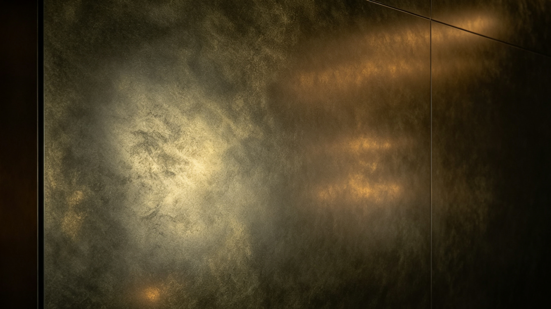 Close-up of a textured, metallic, bronze-colored surface with a matte finish, divided by vertical lines, with a soft glow of light reflecting on it.