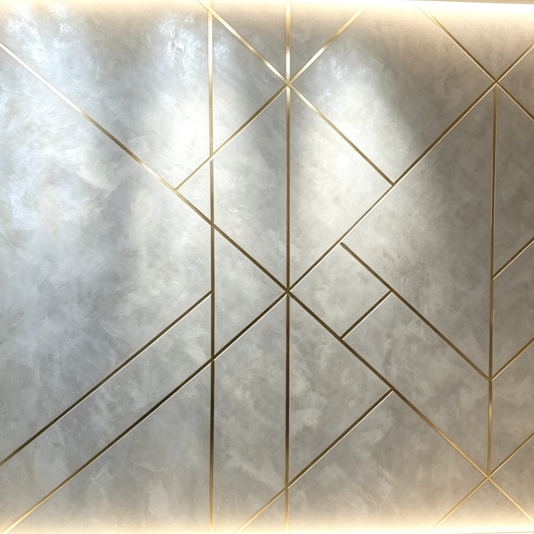 Close-up of a wall with a geometric pattern of gold lines creating diamond shapes, with a textured gray background.