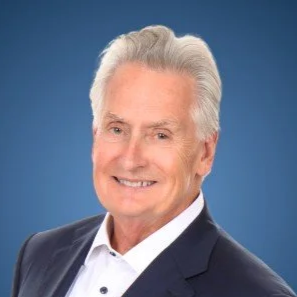 Black and white portrait of a man in a suit and tie, smiling, with a neutral background.