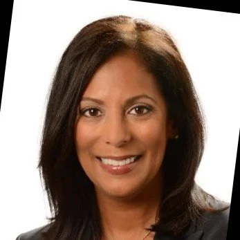 Black and white portrait of a woman with medium-length hair, wearing a blazer and necklace, smiling at the camera.