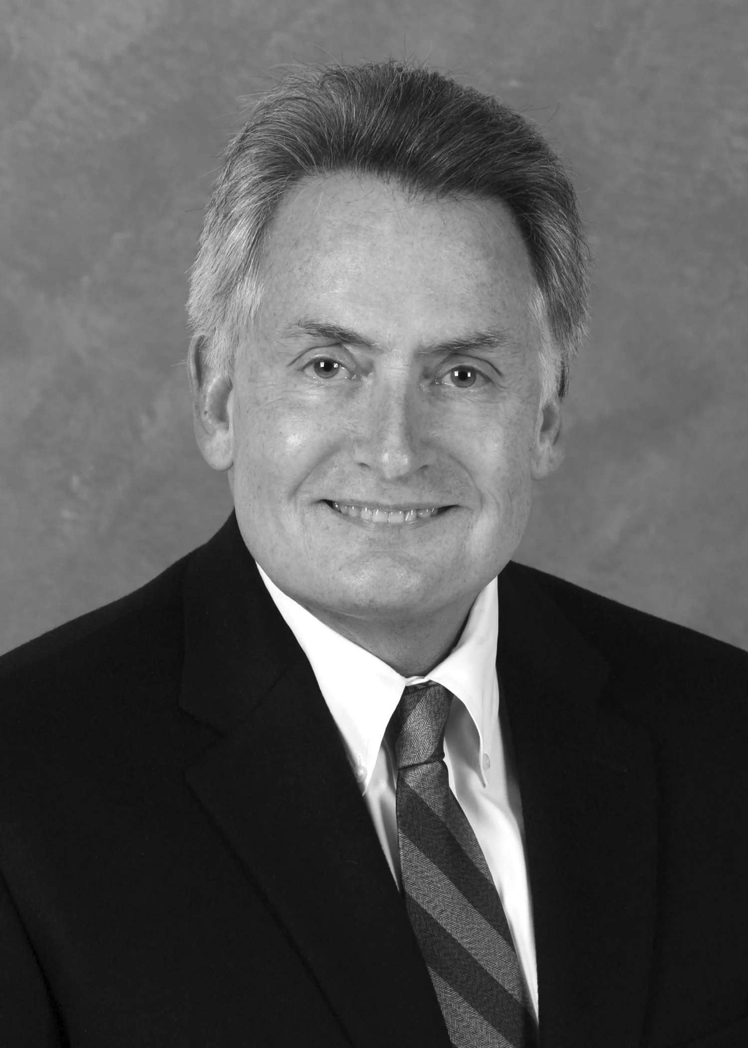 Black and white portrait of a man in a suit and tie, smiling, with a neutral background.