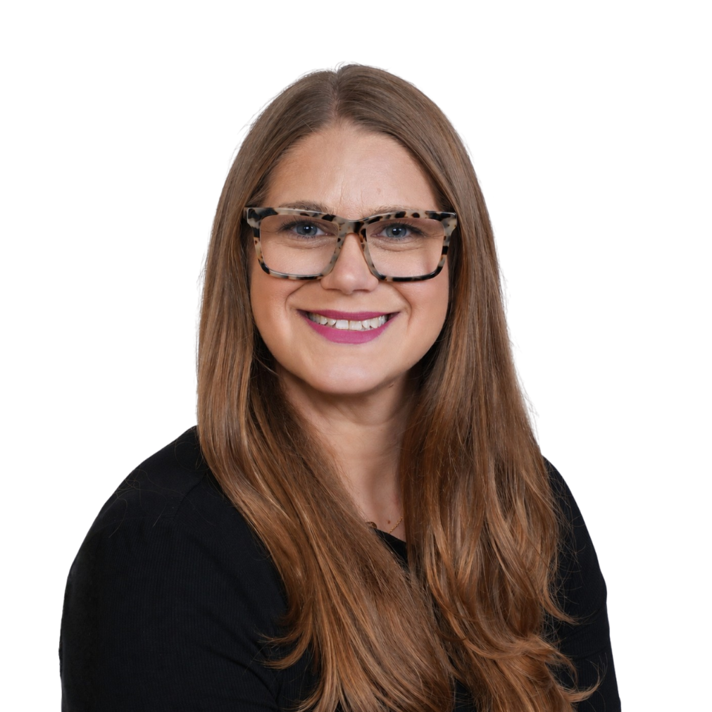 A woman with long reddish hair wearing glasses with a tortoise shell frame, smiling in front of a white background.