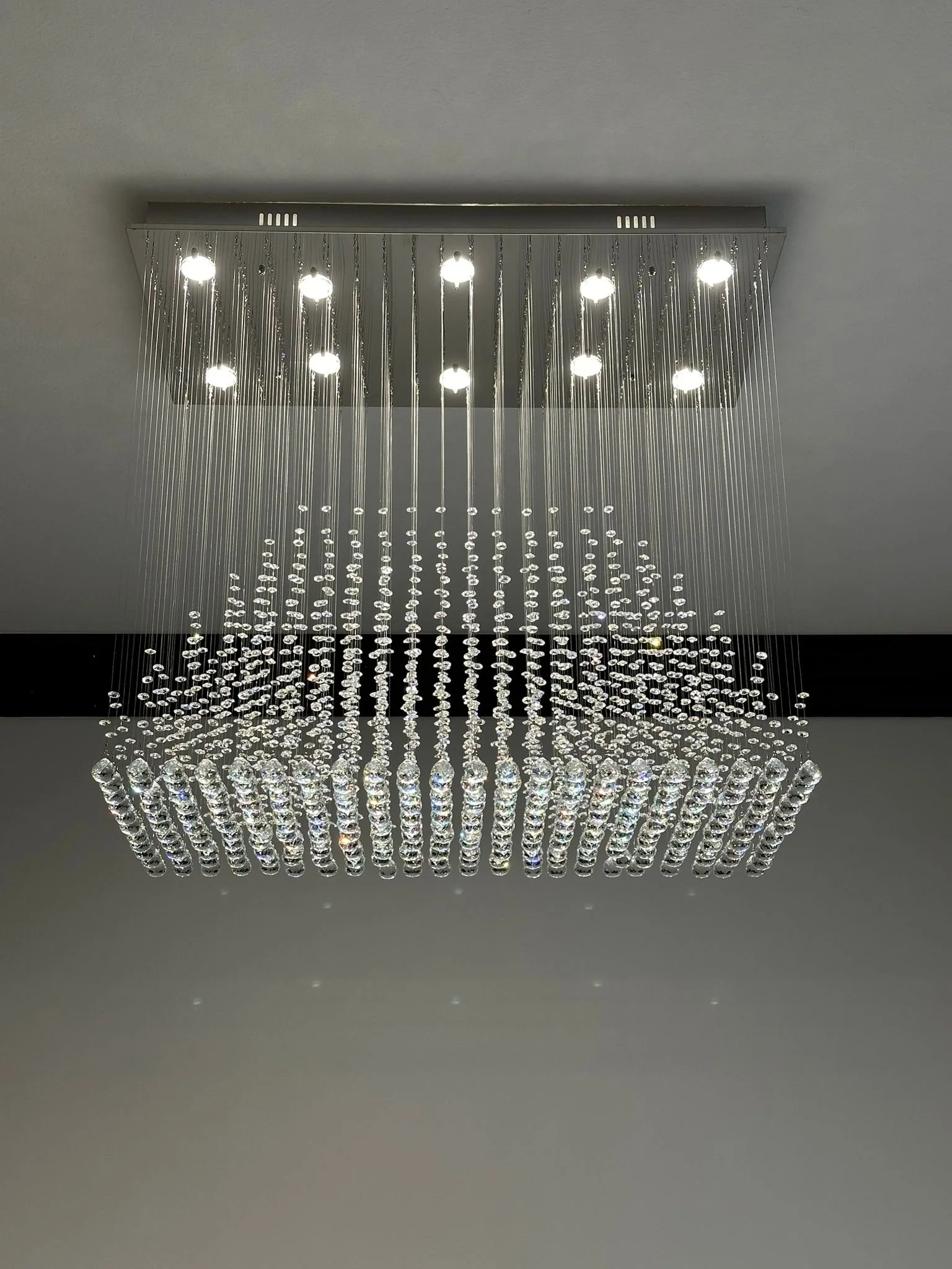 A modern chandelier with numerous crystal hanging decorations and multiple small lights at the top, mounted on a ceiling in a contemporary interior.
