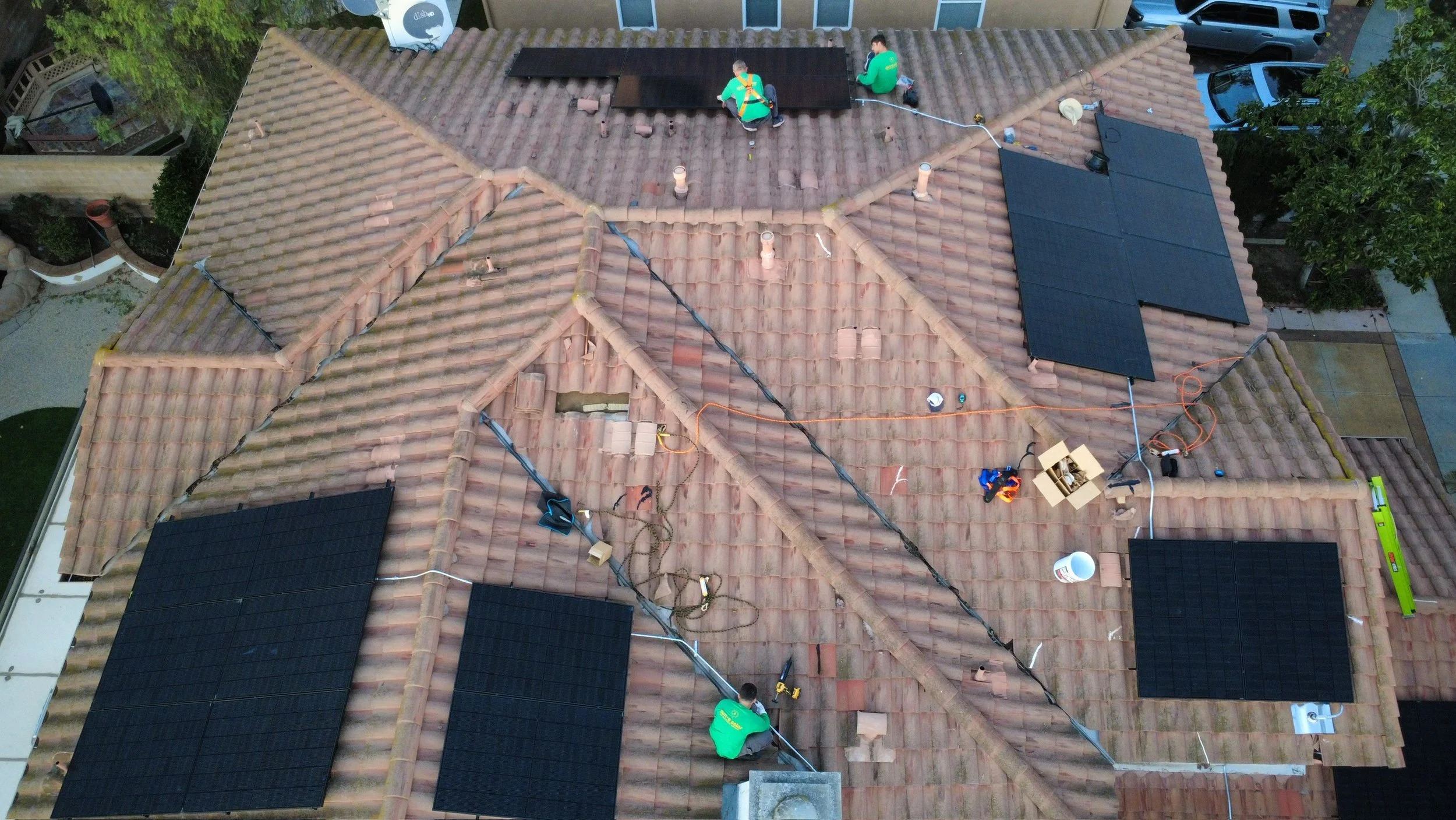 Aerial view of workers installing solar panels on a tiled roof.