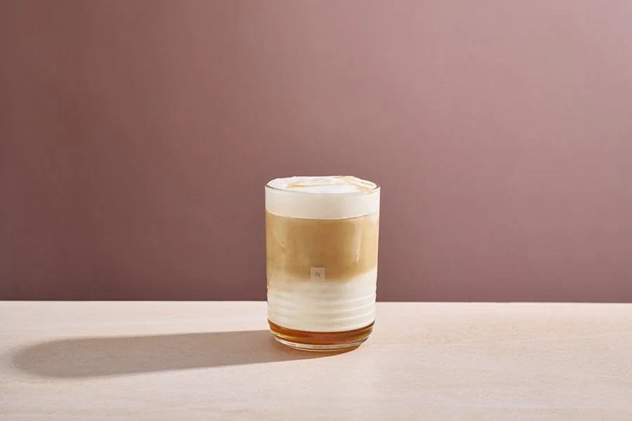 Vaso con café con leche y crema en un fondo rosa