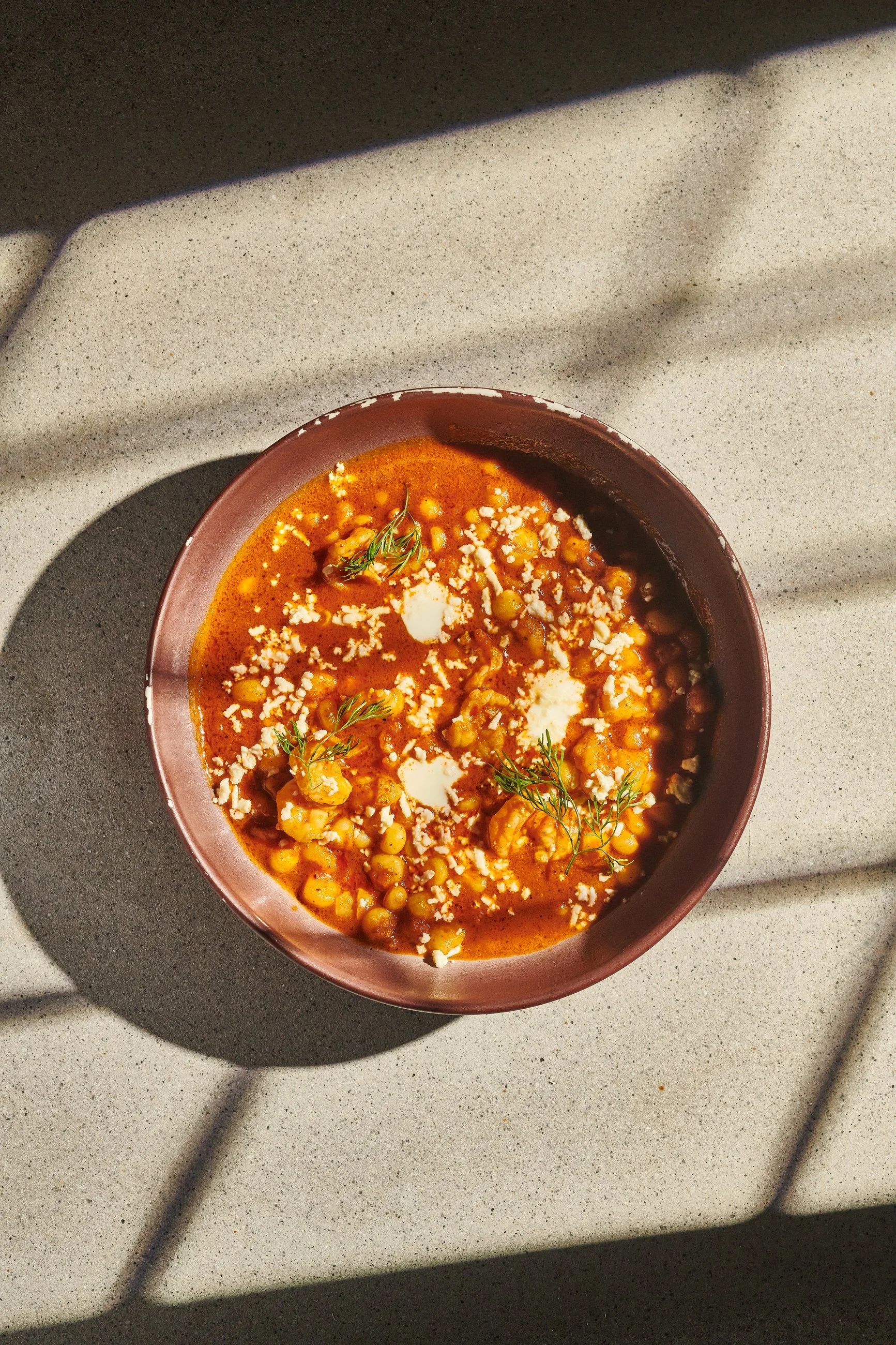 Un tazón de sopa de garbanzos con cilantro y queso en un fondo de superficie gris con sombras