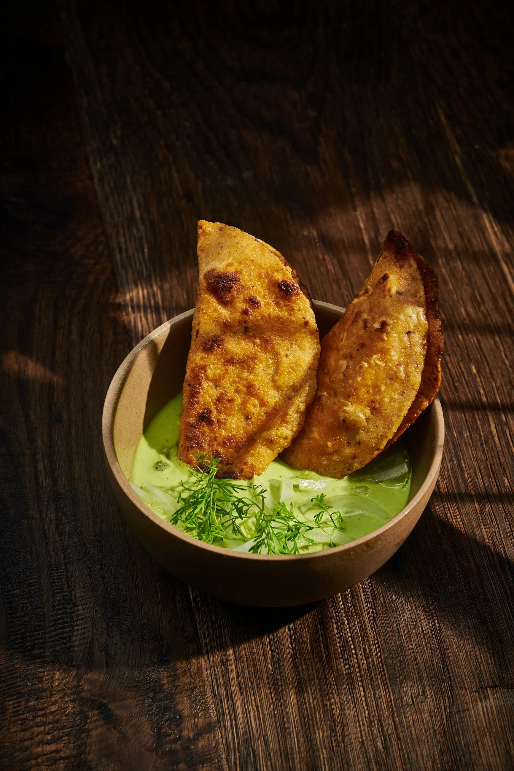 Dos guacamole con totopos en un tazón de cerámica sobre una mesa de madera oscura.