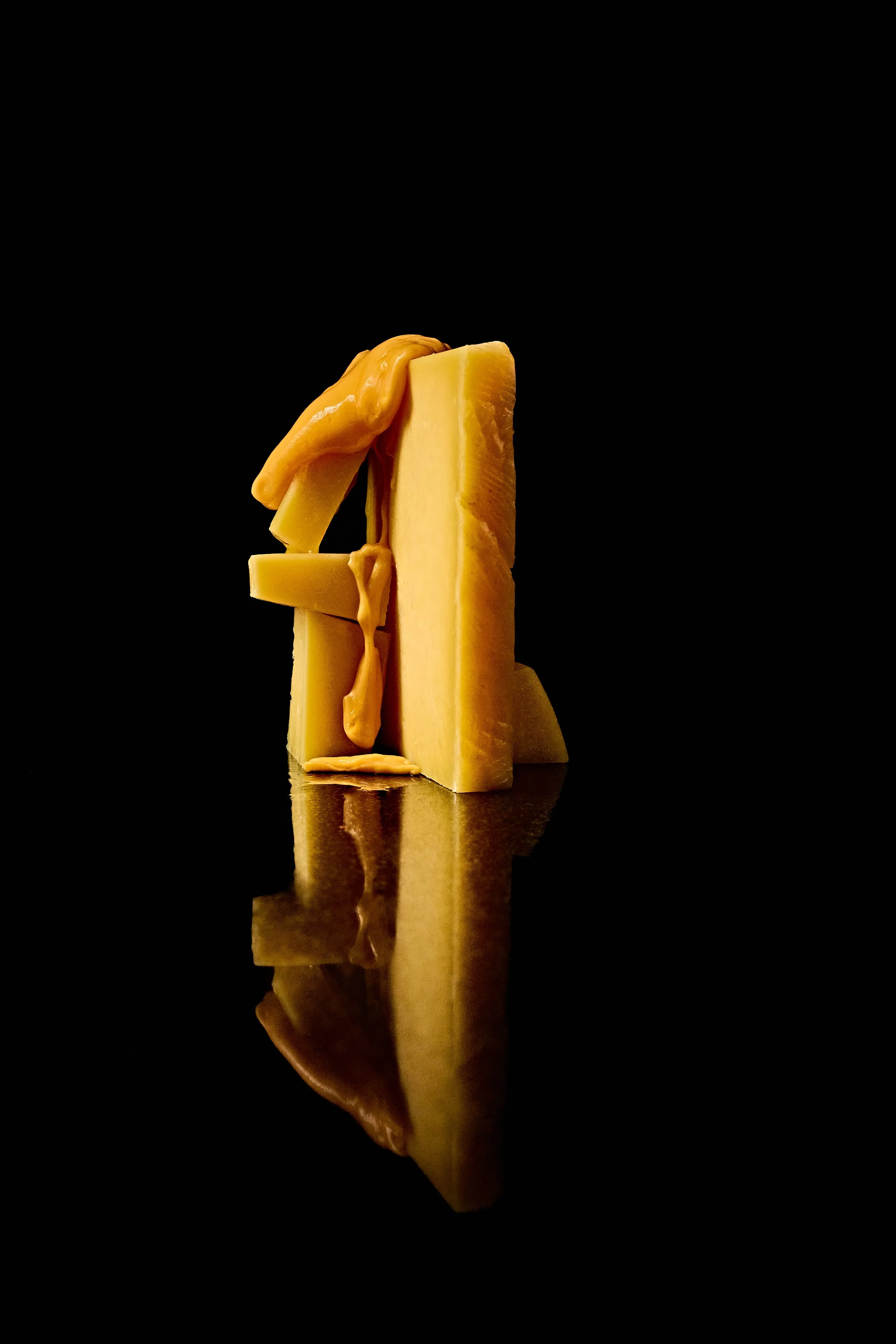 Queso amarillo en trozos con un poco de queso derretido, reflejado en una superficie negra.