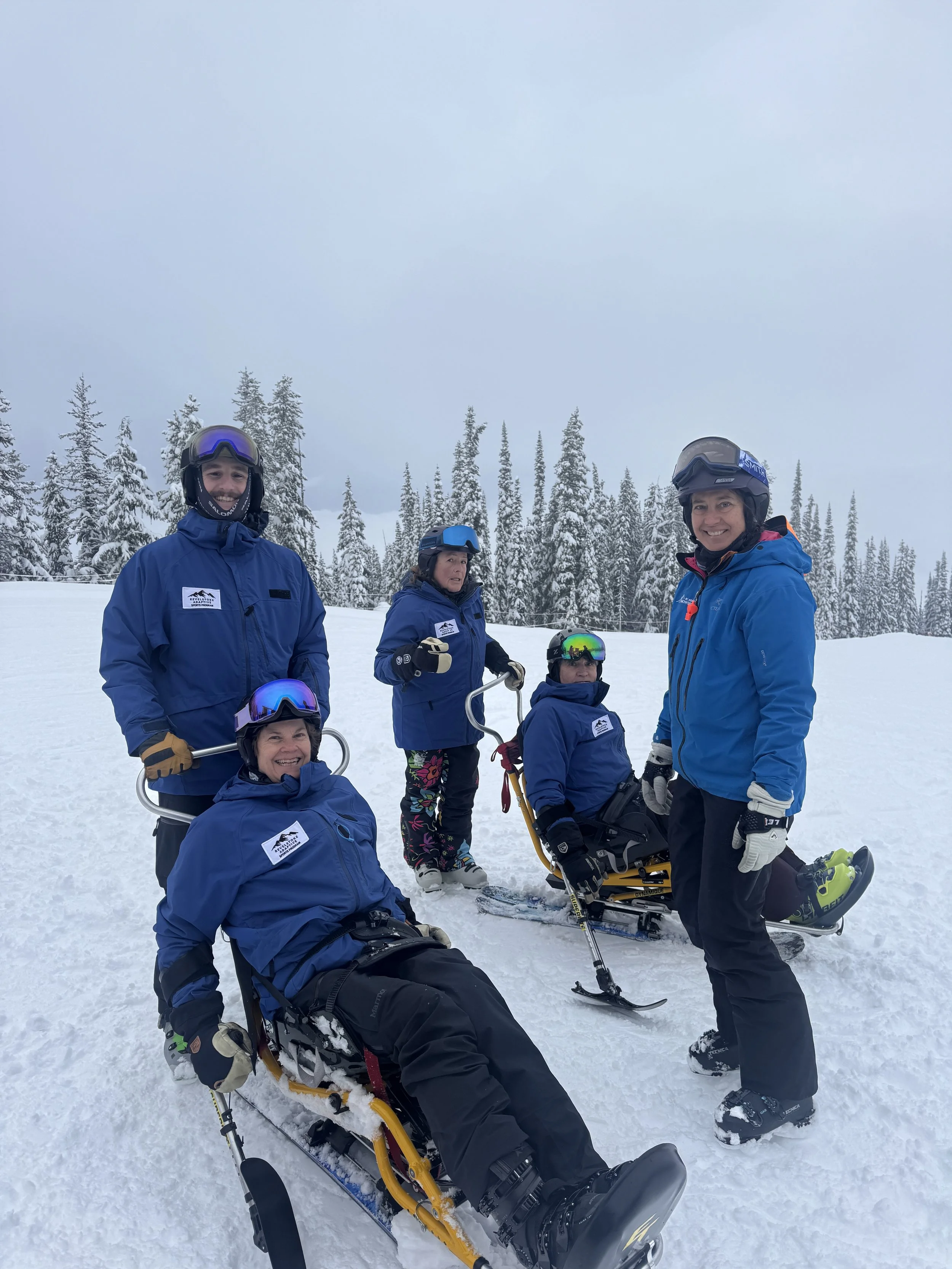 A person in winter gear riding a special ski chair on snow with mountains in the background. There is an orange sign that reads 'The Stoke Chair' with an arrow pointing to the right.